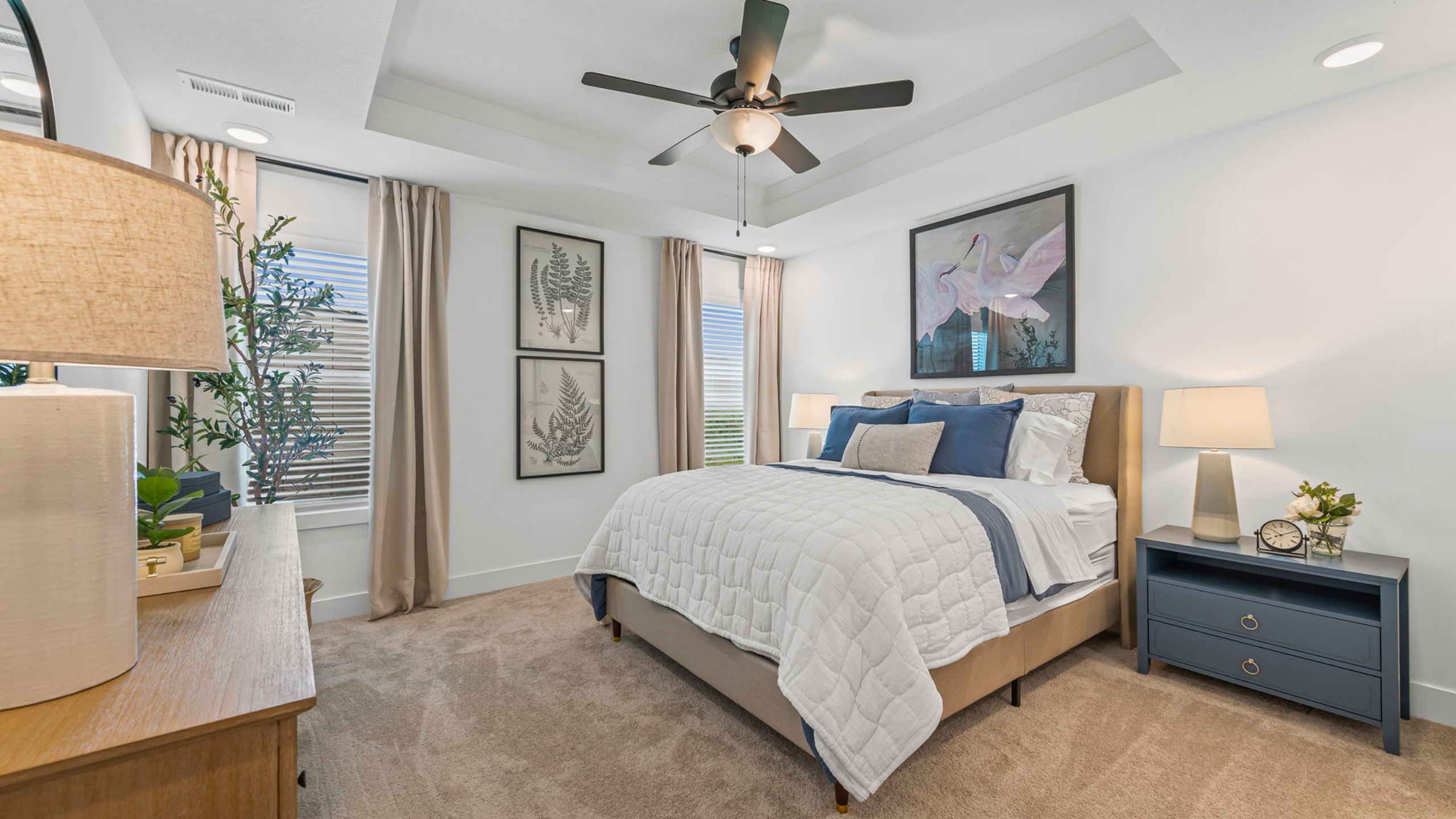 Elegant bedroom with modern decor, featuring a cozy bed, stylish lighting, and serene artwork. Natural light flows through large windows with tasteful curtains.