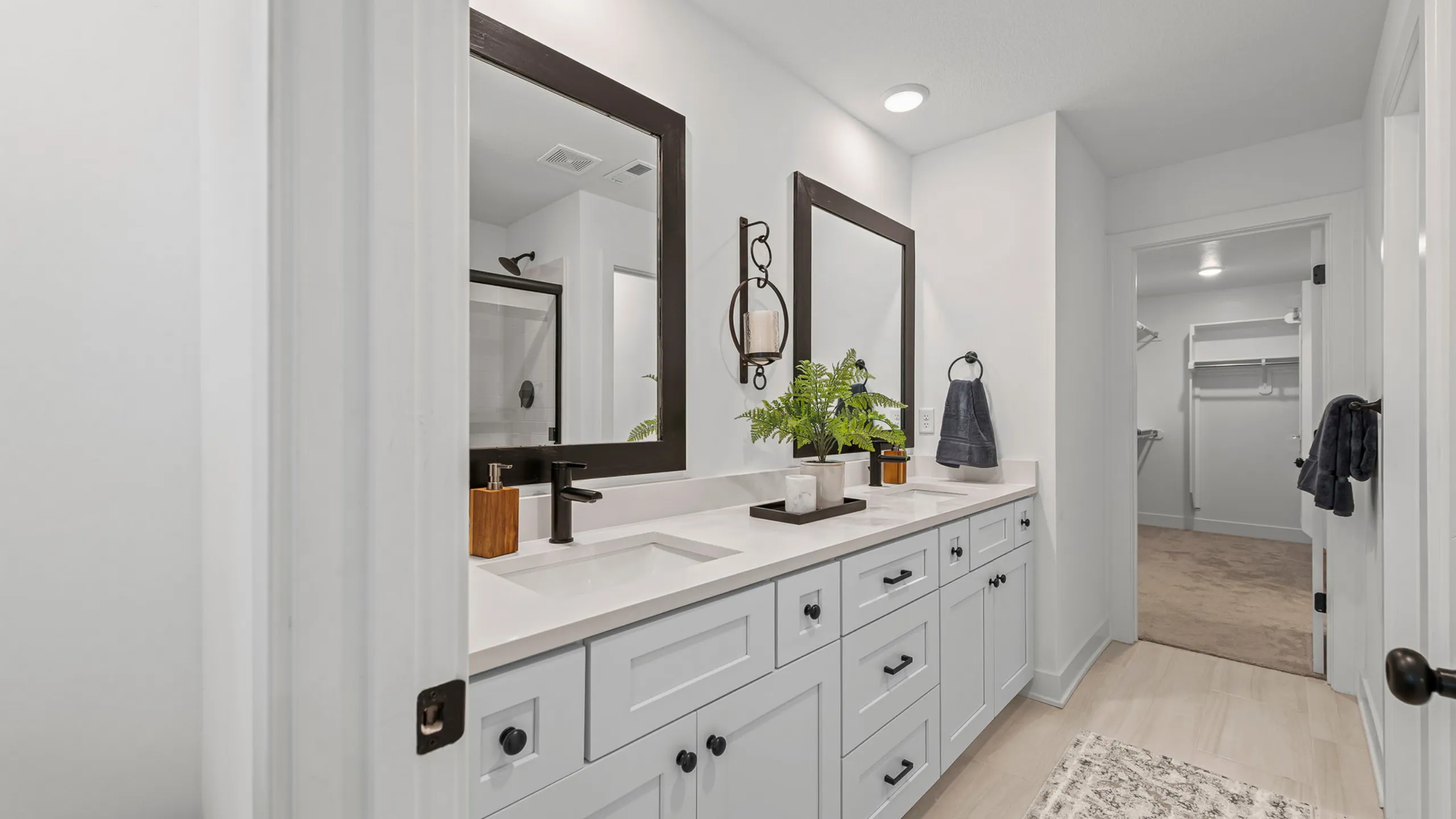 Luxurious bathroom with dual sinks, elegant mirrors, and a sleek modern design leading to a spacious walk-in closet.