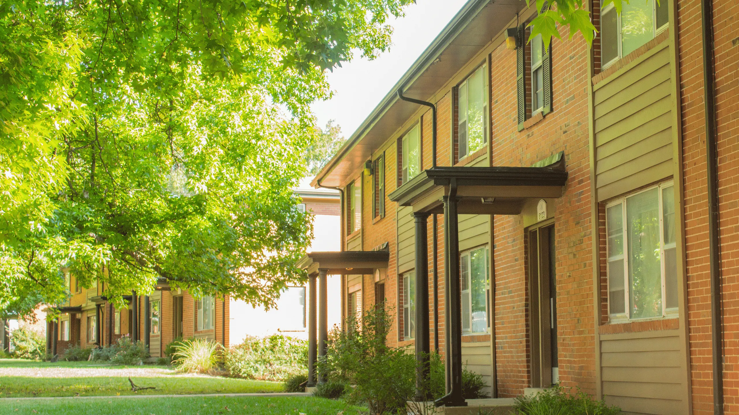 Charming brick apartment complex nestled under lush green trees, offering a serene and welcoming atmosphere.