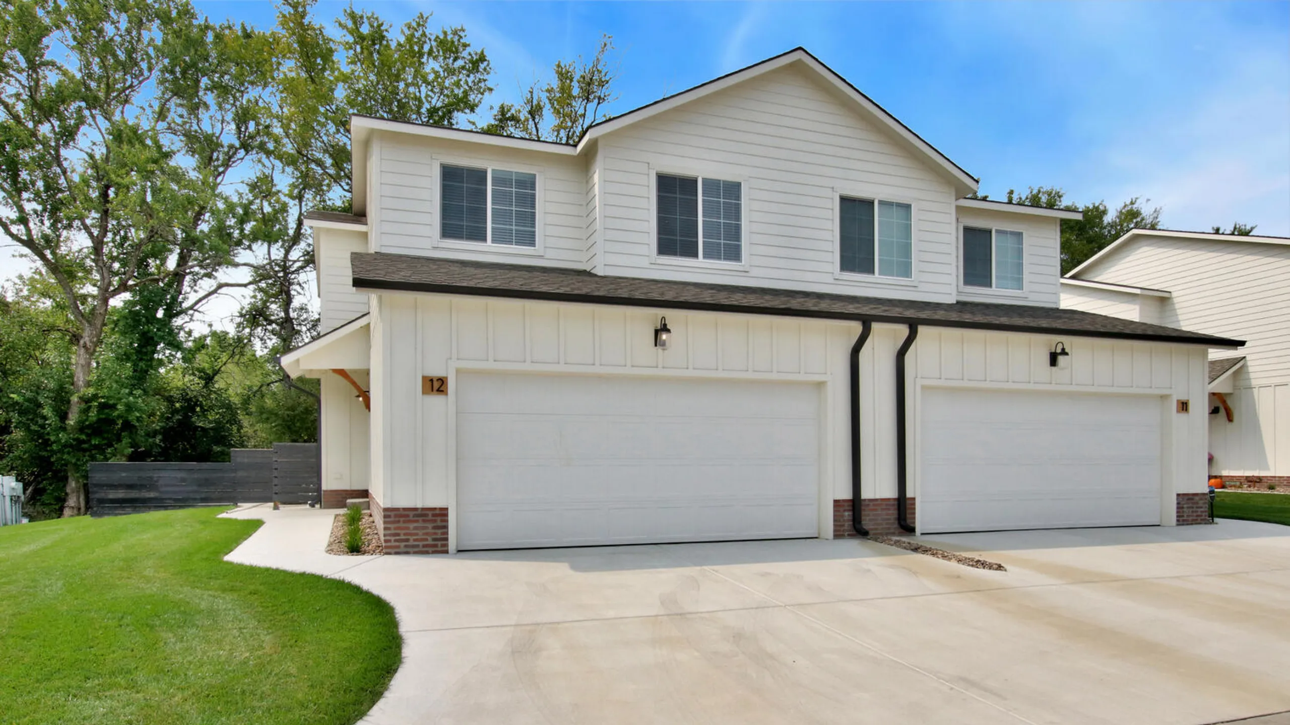 Charming duplex with modern white facade, spacious two-car garage, and lush green surroundings, perfect family living.