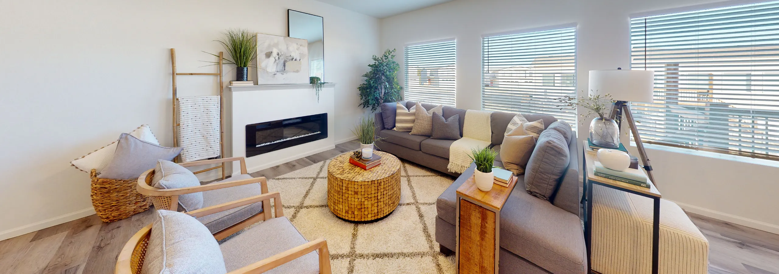 Inviting living room with ample natural light, featuring a cozy gray sectional, elegant fireplace, and contemporary decor for a warm ambience.