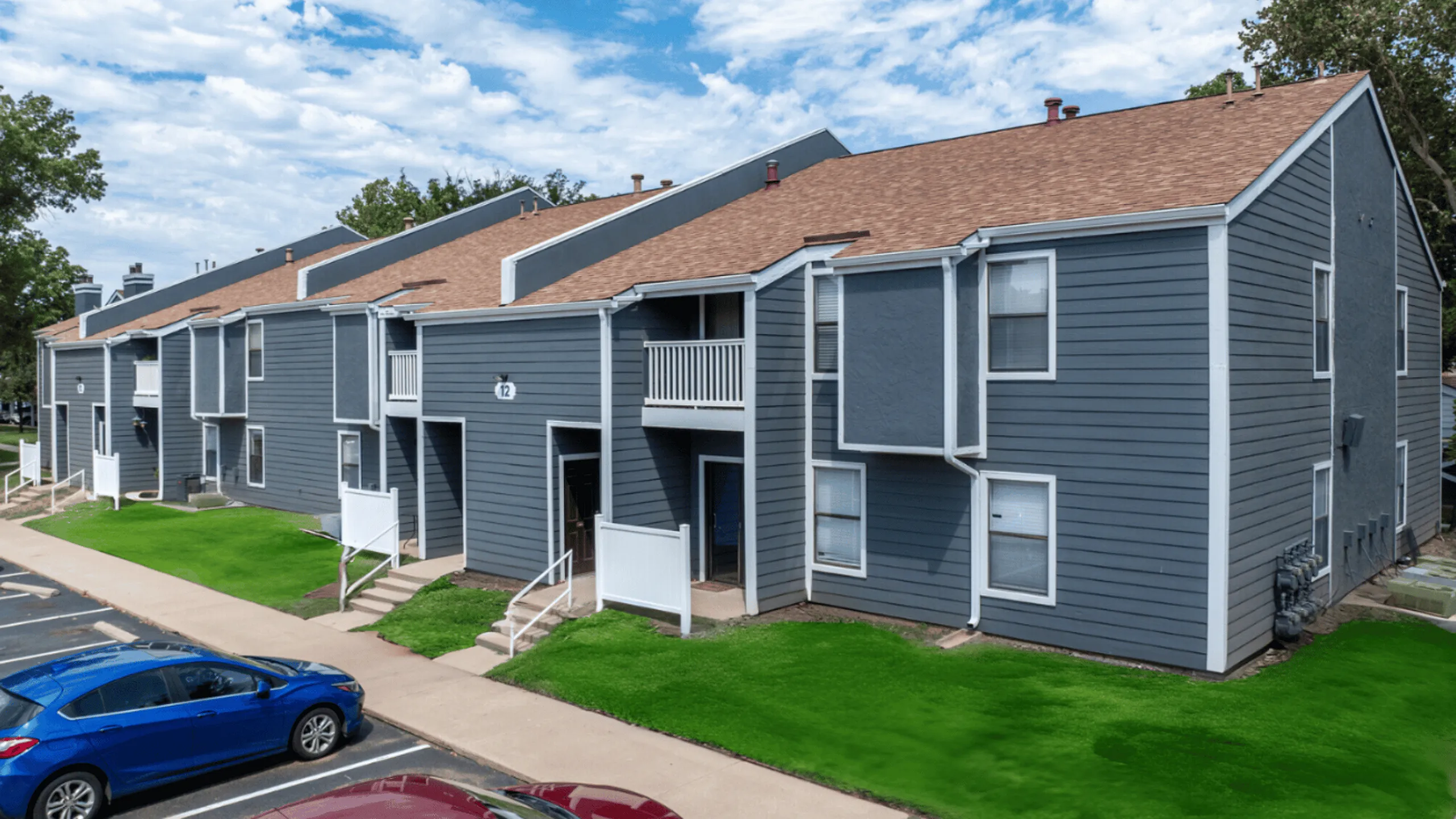 Charming blue-gray apartment complex with multiple units, fresh green landscaping, and spacious balconies, perfect for modern living.