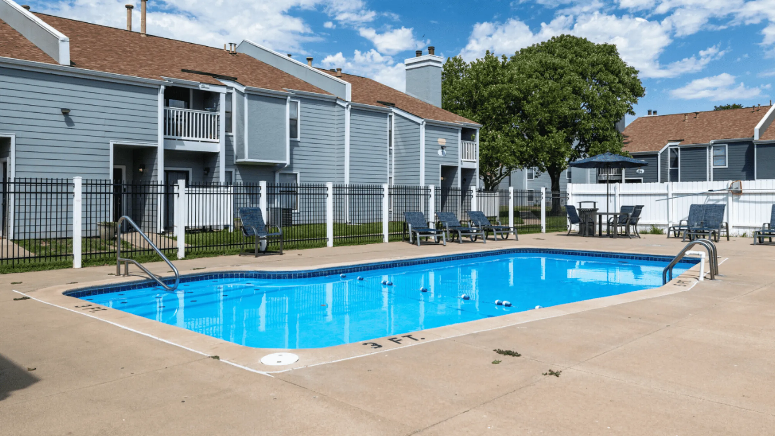 Inviting apartment complex featuring a sparkling swimming pool, surrounded by a spacious sun deck and modern lounge chairs.