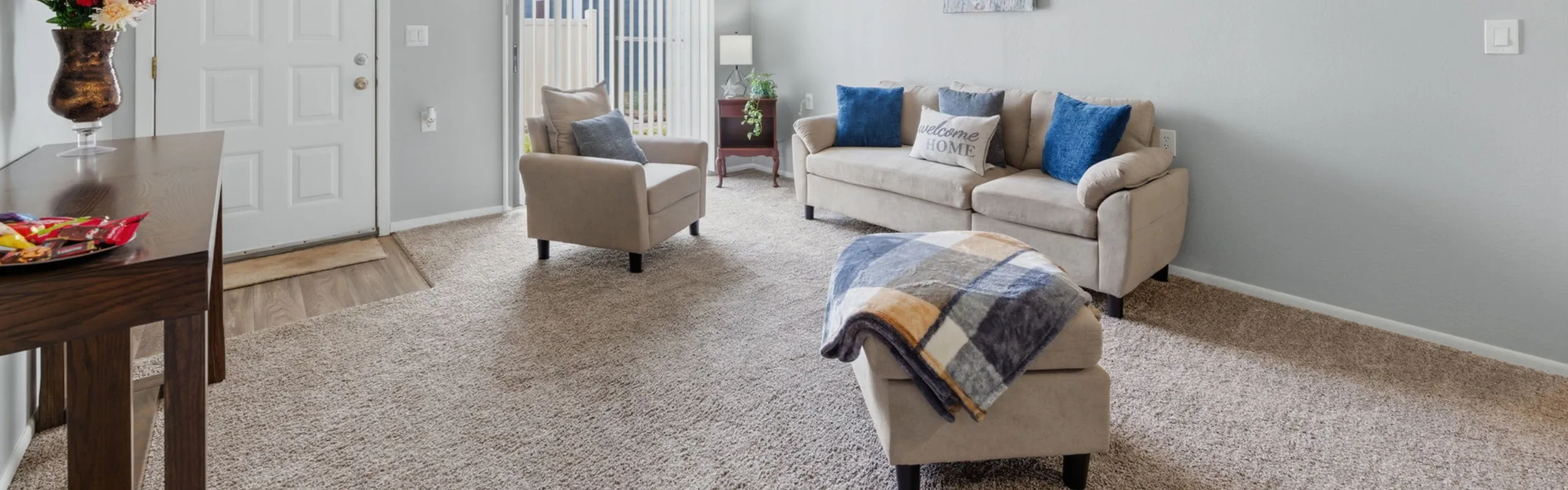 Inviting living room with cozy beige sofa, accented by vibrant blue pillows, a chic armchair, and a plush carpet, perfect for relaxation.