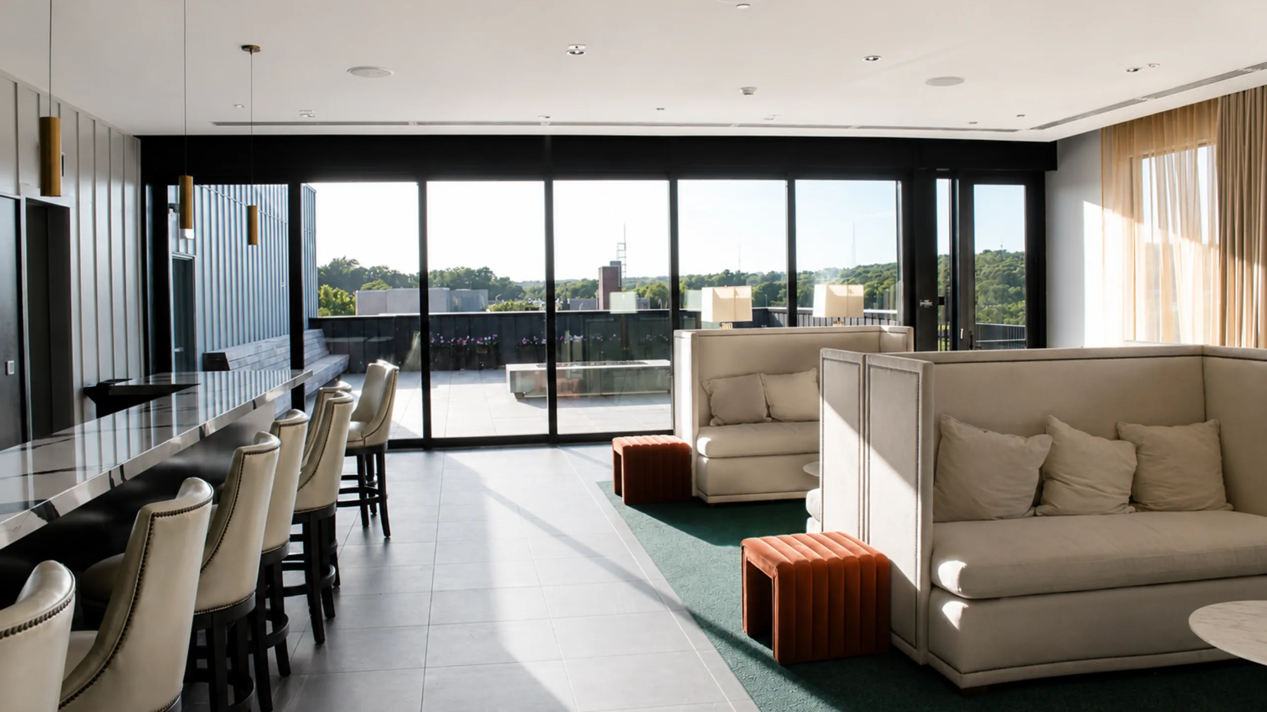Modern lounge area with floor-to-ceiling windows offering a panoramic view, featuring sleek bar seating and cozy sofas, perfect for relaxation and entertaining.