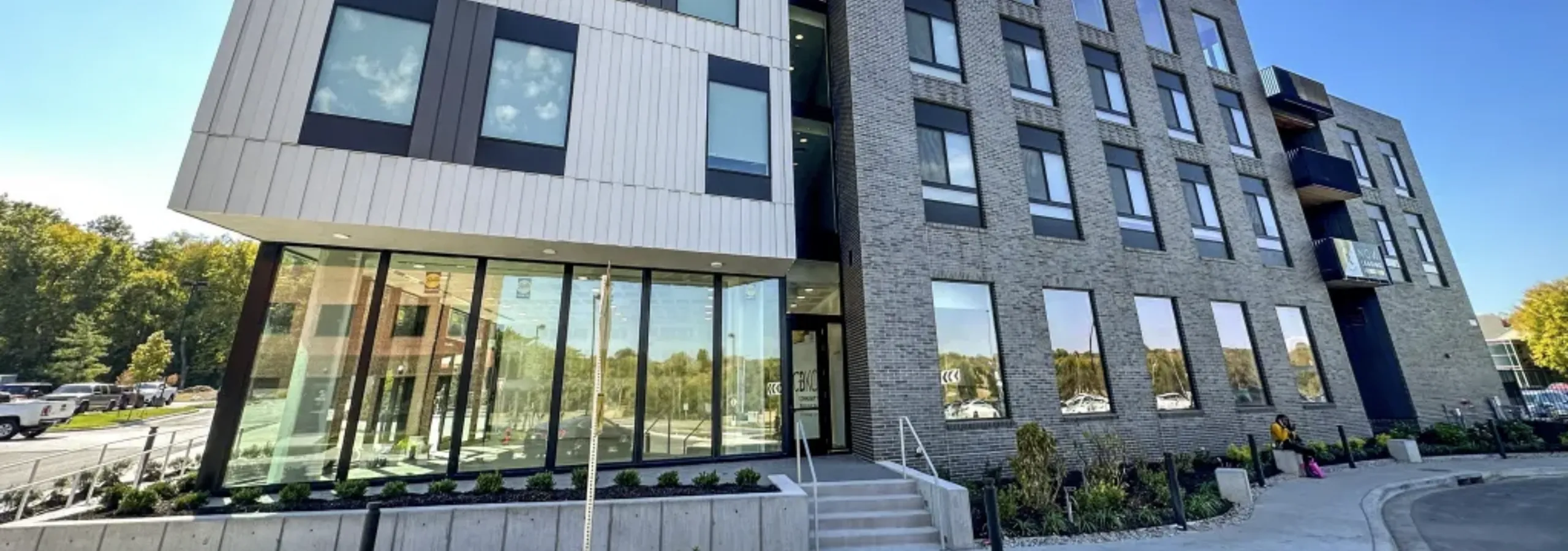 Contemporary apartment building with sleek glass and brick facade, featuring large windows and modern landscaping.