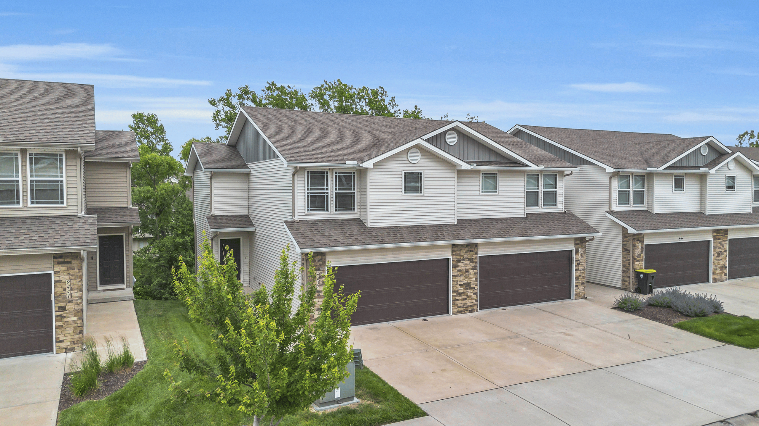Charming two-story townhouse with modern design, featuring double garages and surrounded by lush greenery in a quiet suburban neighborhood.