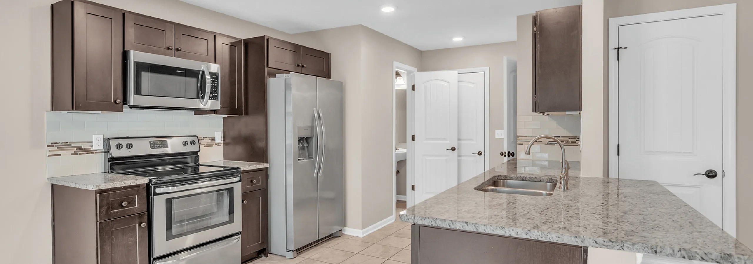 Modern kitchen with sleek stainless steel appliances, dark wood cabinets, and elegant granite countertops.