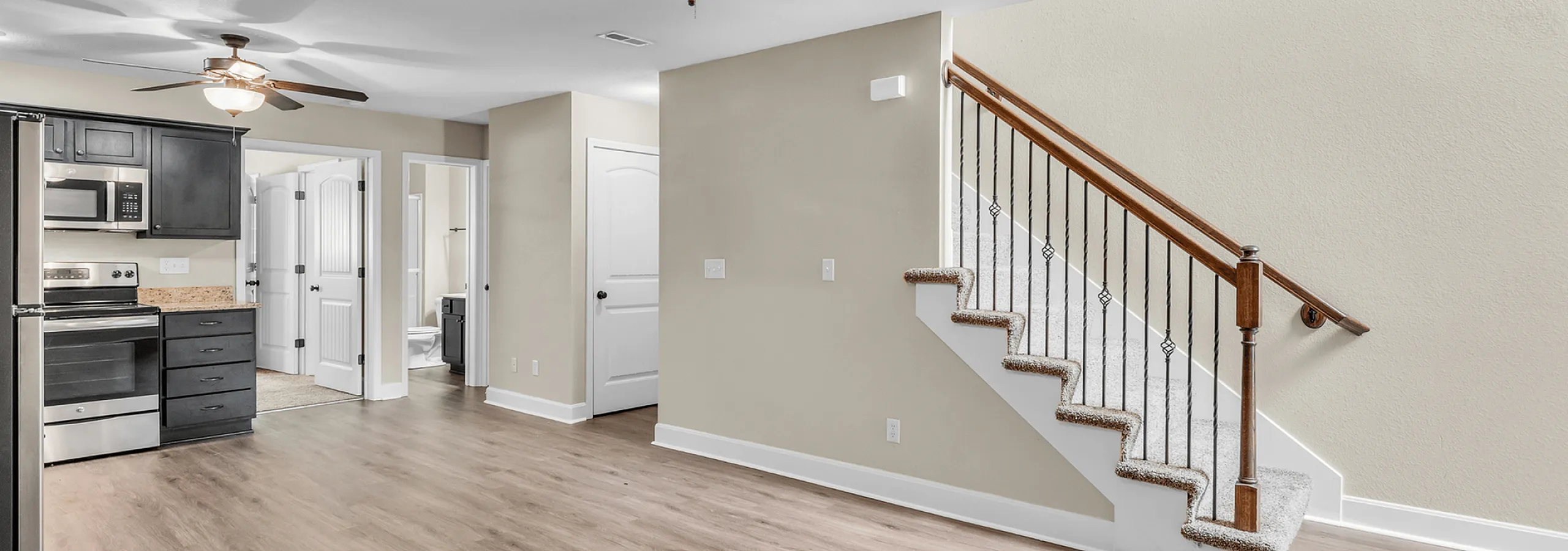 Modern apartment interior with sleek kitchen, stainless steel appliances, and elegant staircase leading to upper level.