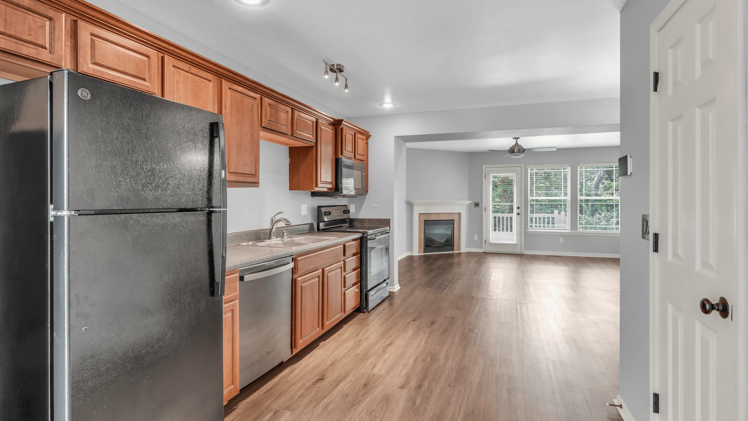 Modern kitchen with stainless steel appliances and wood cabinetry opens into a bright living area with large windows and cozy fireplace.