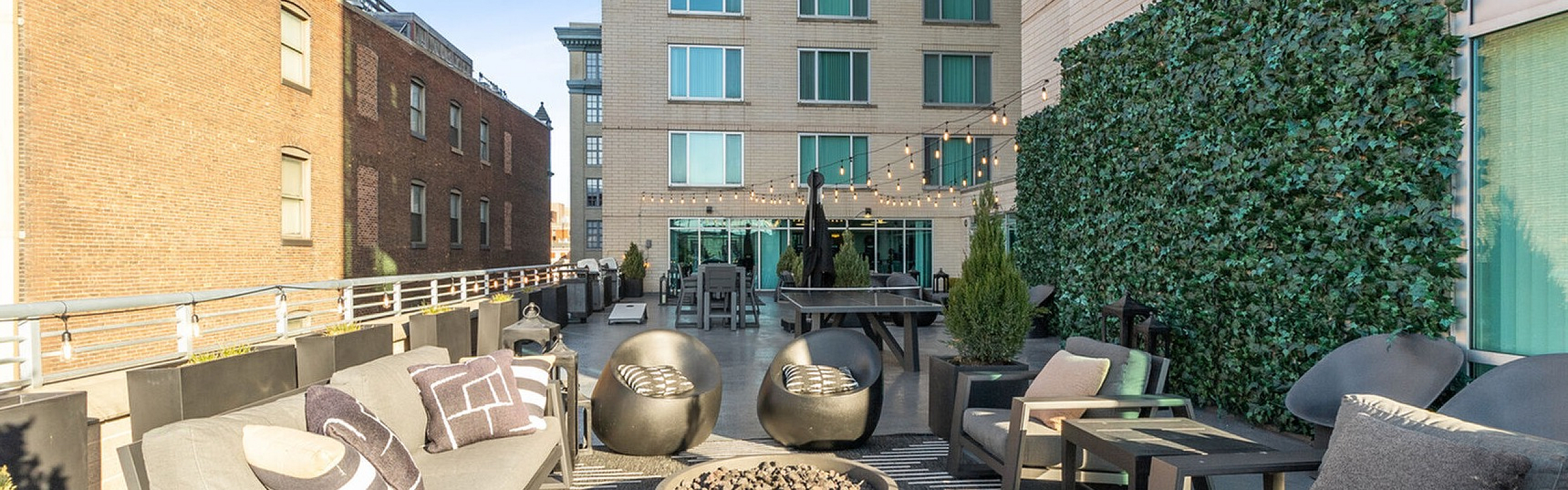 Chic urban patio with cozy seating, string lights, and lush greenery, perfect for relaxation and entertaining.