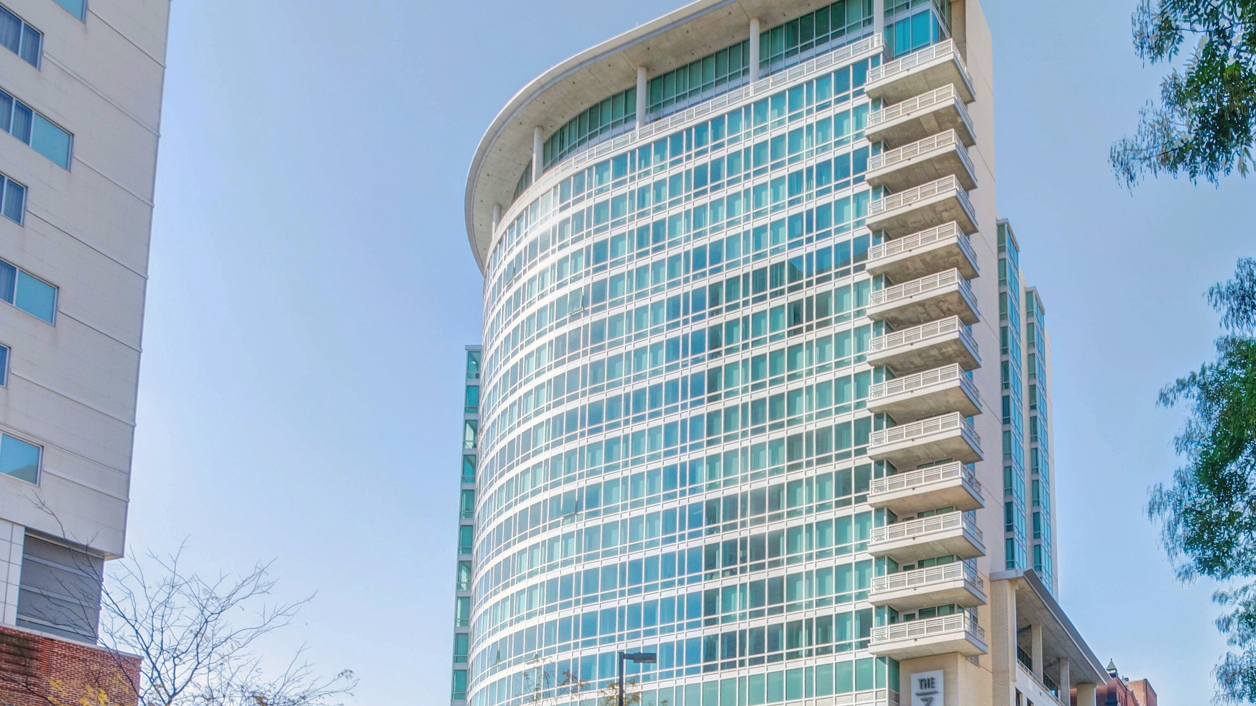 Modern high-rise building with sleek glass facade and balconies, set against a clear blue sky.