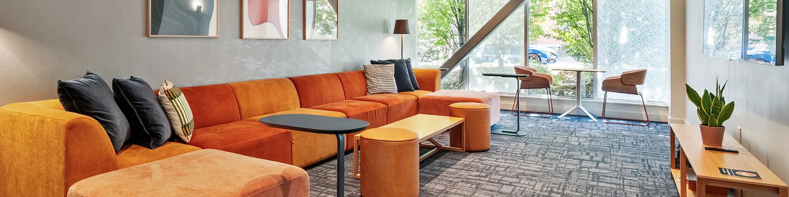 Modern living room with vibrant orange sectional sofa, sleek decor, and large windows offering lush garden views.