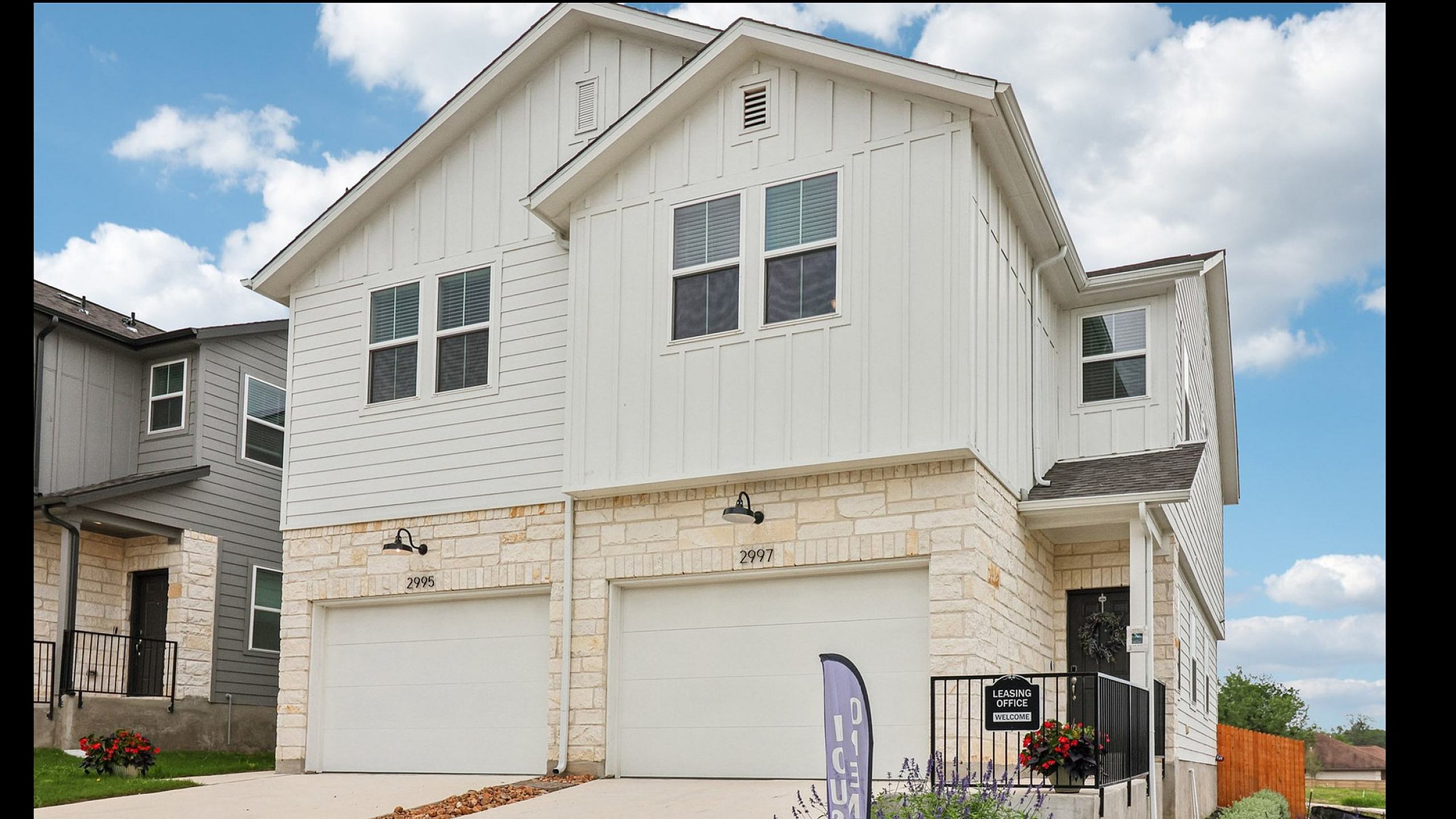 Charming modern duplex with white exterior, two-car garages, and inviting entryway, set against a bright blue sky.