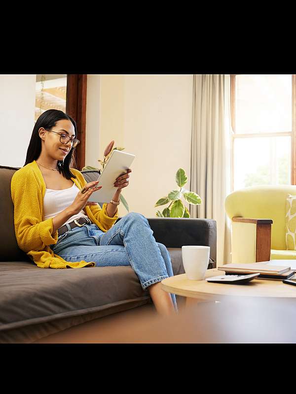 Bright and cozy living room with a stylish young woman relaxing on a comfortable sofa, enjoying natural light from large windows.
