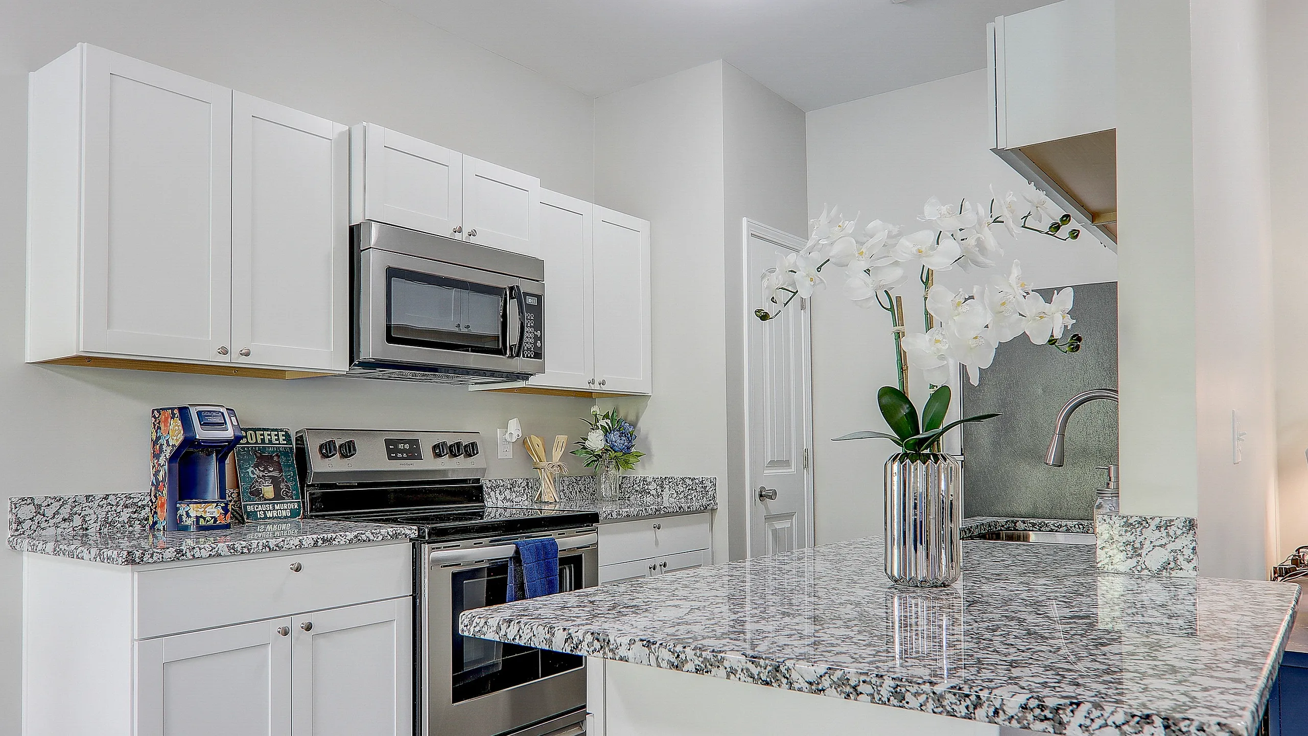 Elegant kitchen with sleek granite countertops, stainless steel appliances, and crisp white cabinetry, accented by vibrant floral decor for a modern touch.