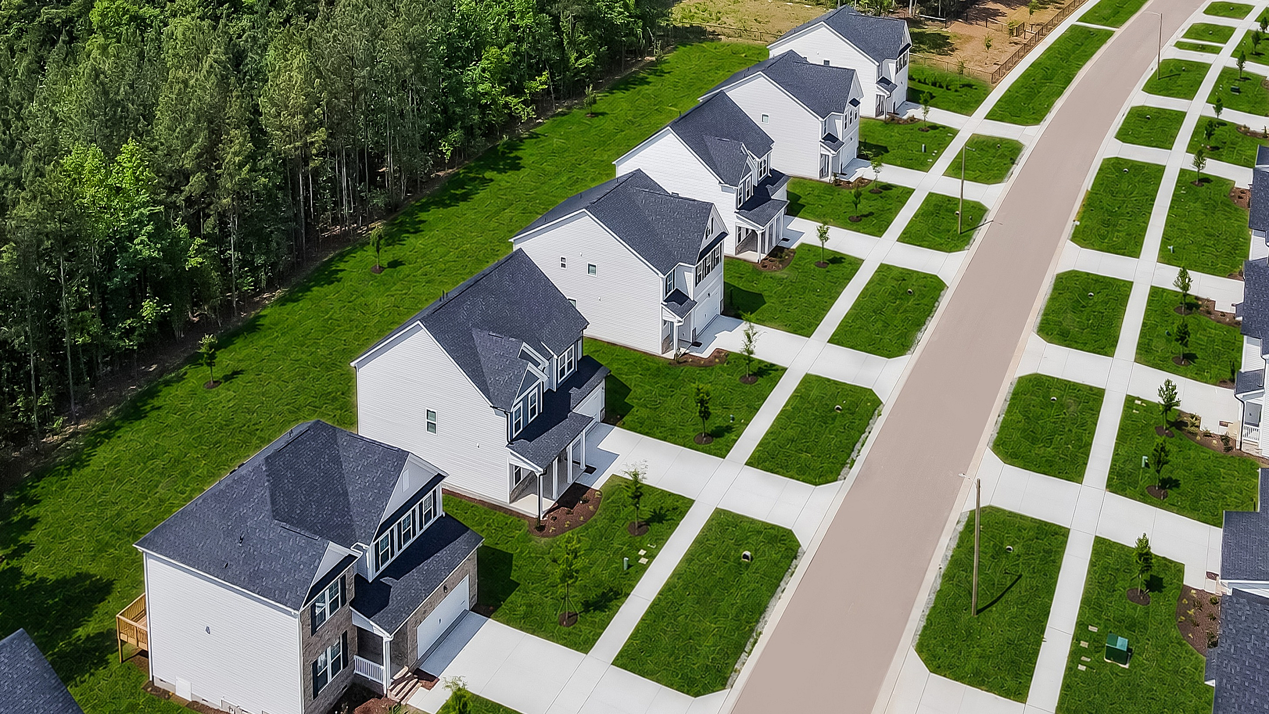 Aerial view of a charming suburban neighborhood with rows of modern homes, neatly manicured lawns, and lush green forestry in the backdrop.