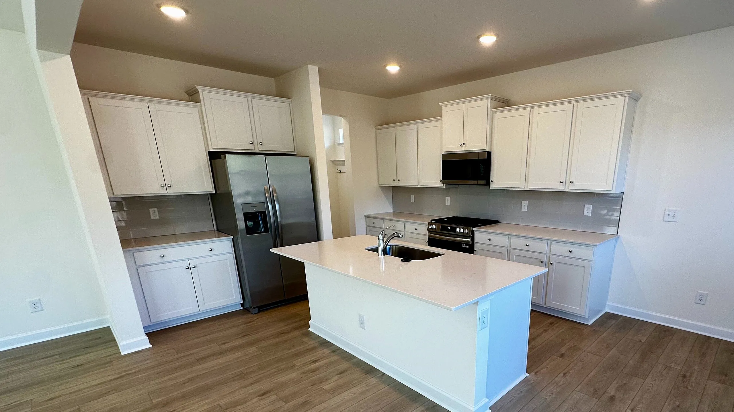 Spacious and modern kitchen with sleek white cabinetry, stainless steel appliances, and elegant wooden flooring.