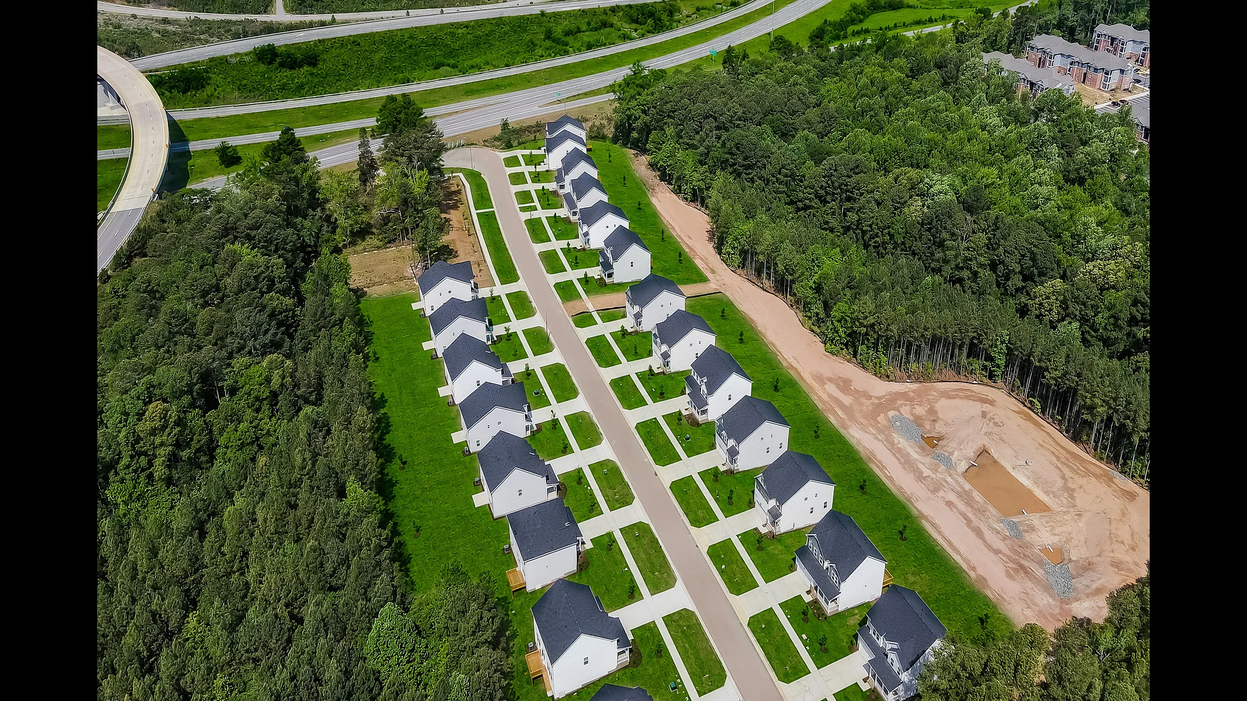 Charming aerial view of a modern suburban neighborhood featuring neat rows of stylish white houses with dark roofs, surrounded by lush greenery and accessible roads.