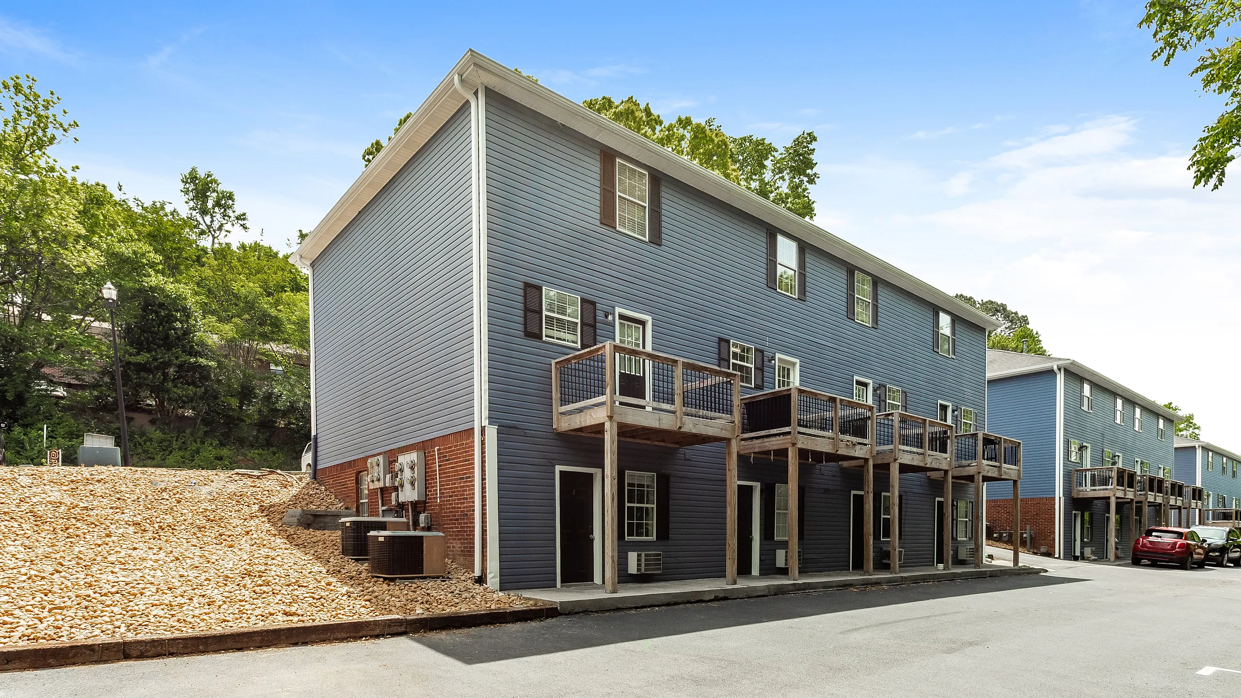 Charming townhouse complex featuring modern blue siding, individual balconies, and scenic wooded backdrop, perfect for comfortable living.