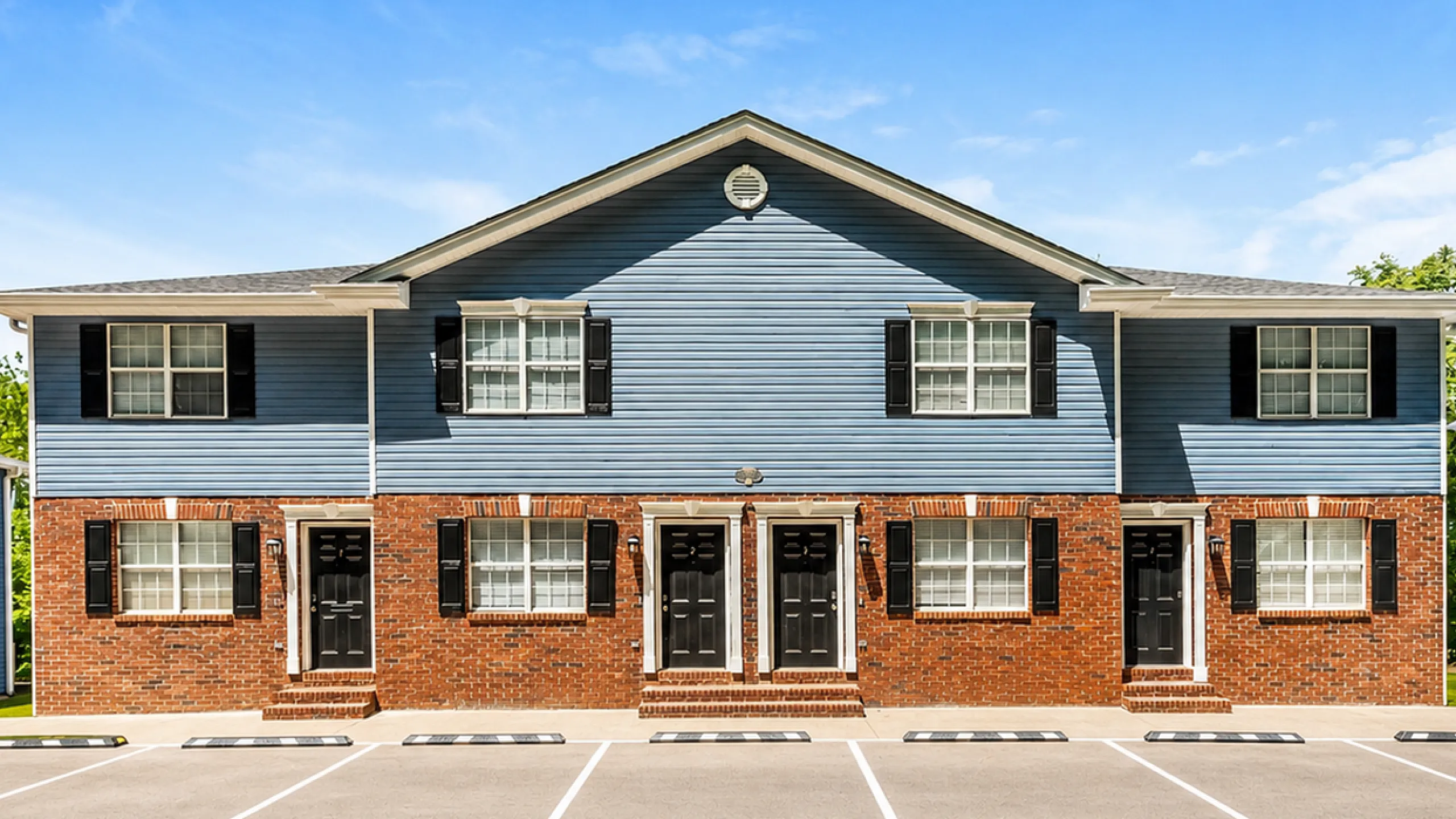 Charming townhouse facade with modern blue siding, brick accents, and ample parking, under a brilliantly clear sky.