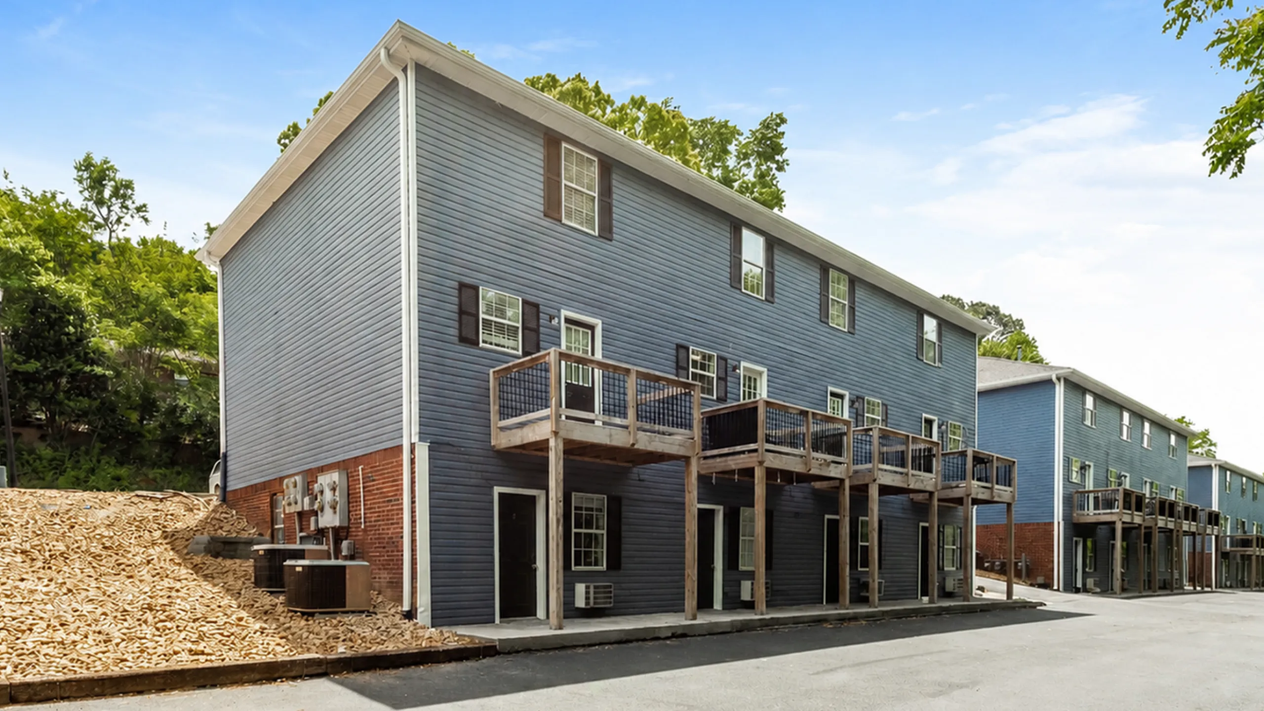 Modern apartment building with stylish wood accents against a serene blue sky, nestled in lush greenery.