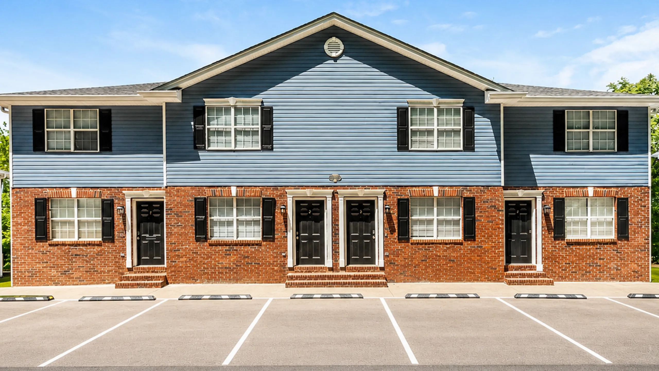 Charming two-story townhouse with blue siding and brick accents, featuring modern windows and inviting entrances, situated in a bright and spacious community.