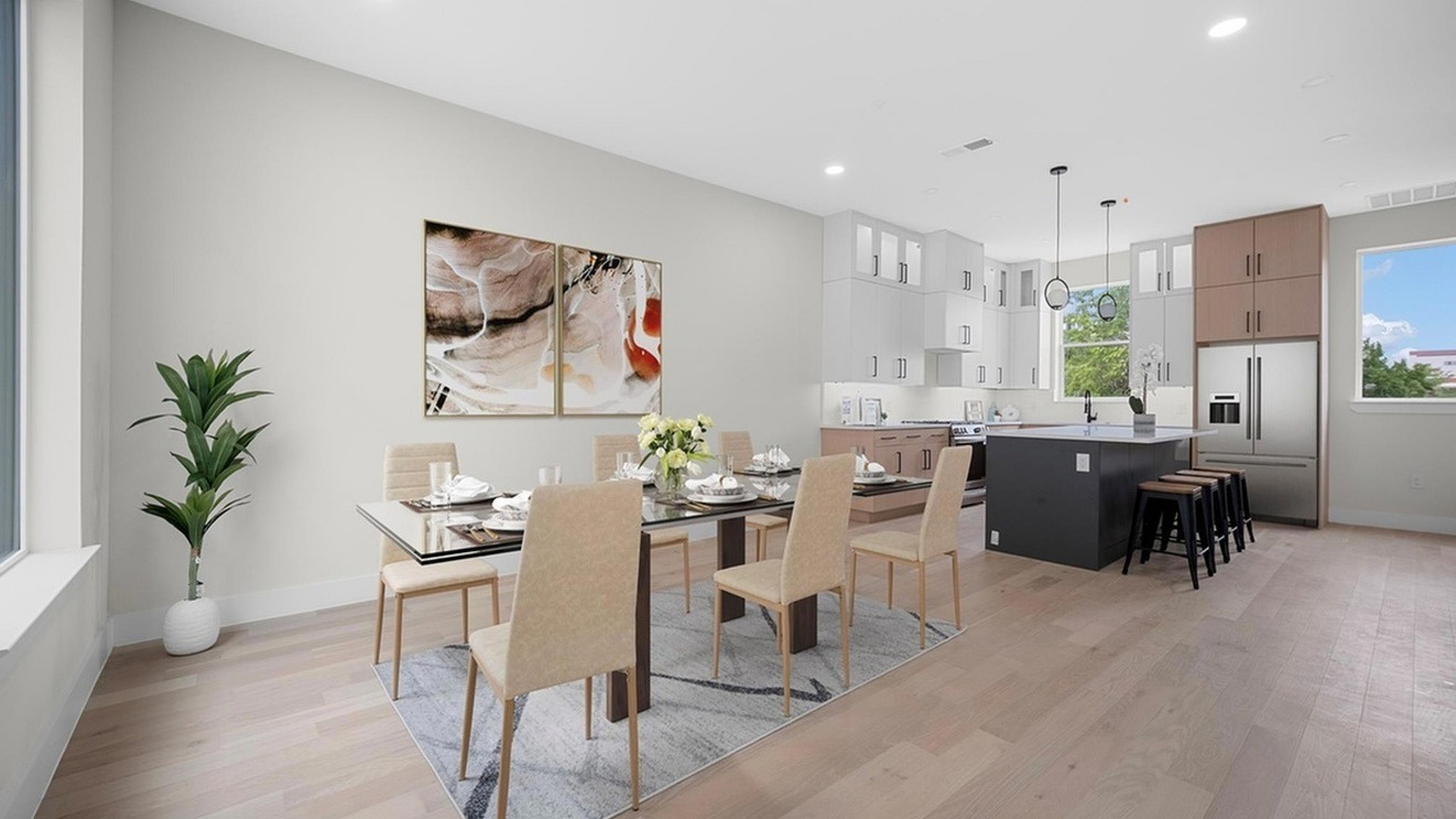 Elegant open-plan dining and kitchen area with modern furnishings, featuring a stylish table set for six, contemporary artwork, and large windows with natural light.