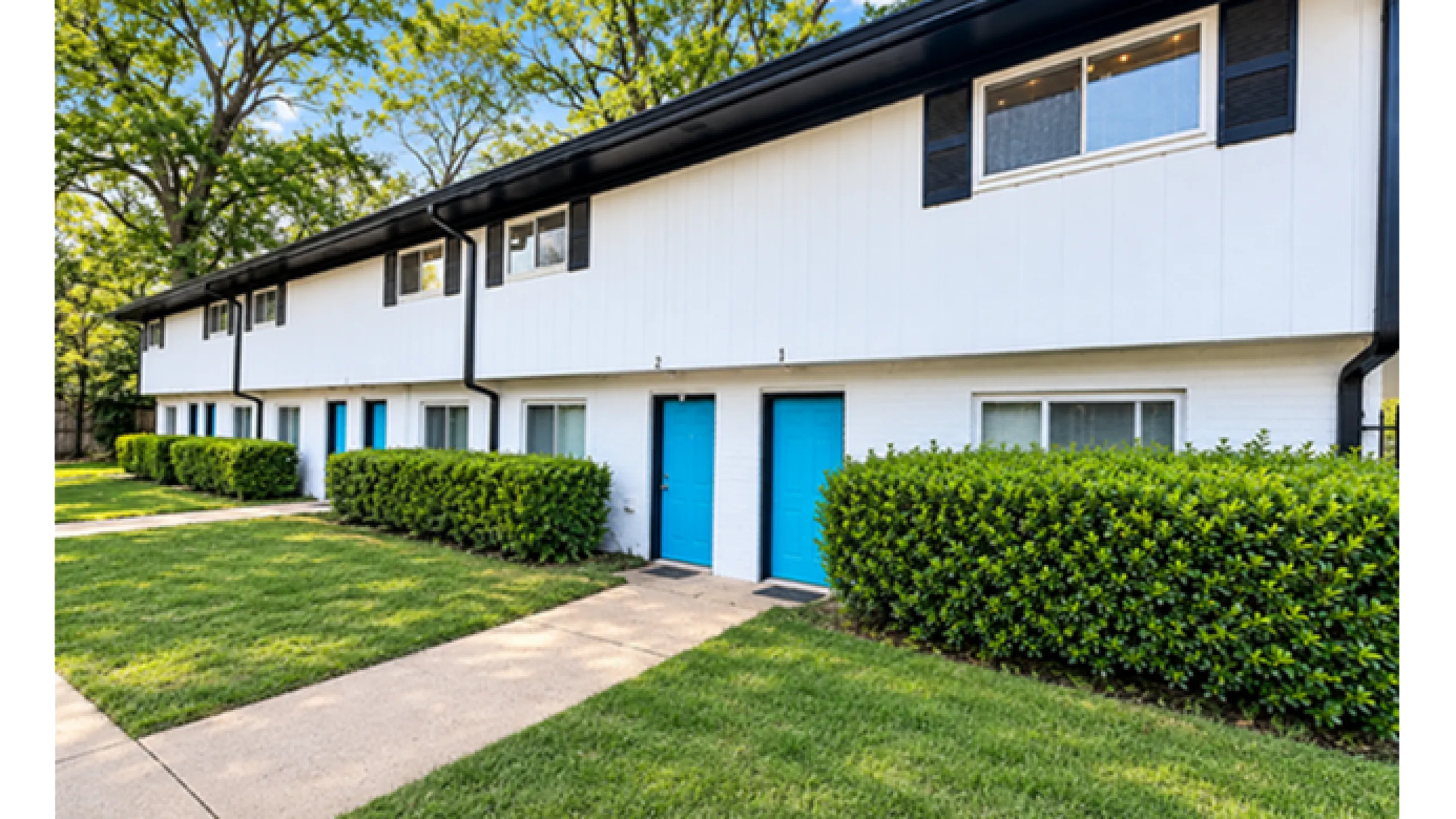 Charming townhouse exterior with vibrant blue doors, lush greenery, and well-maintained lawn.