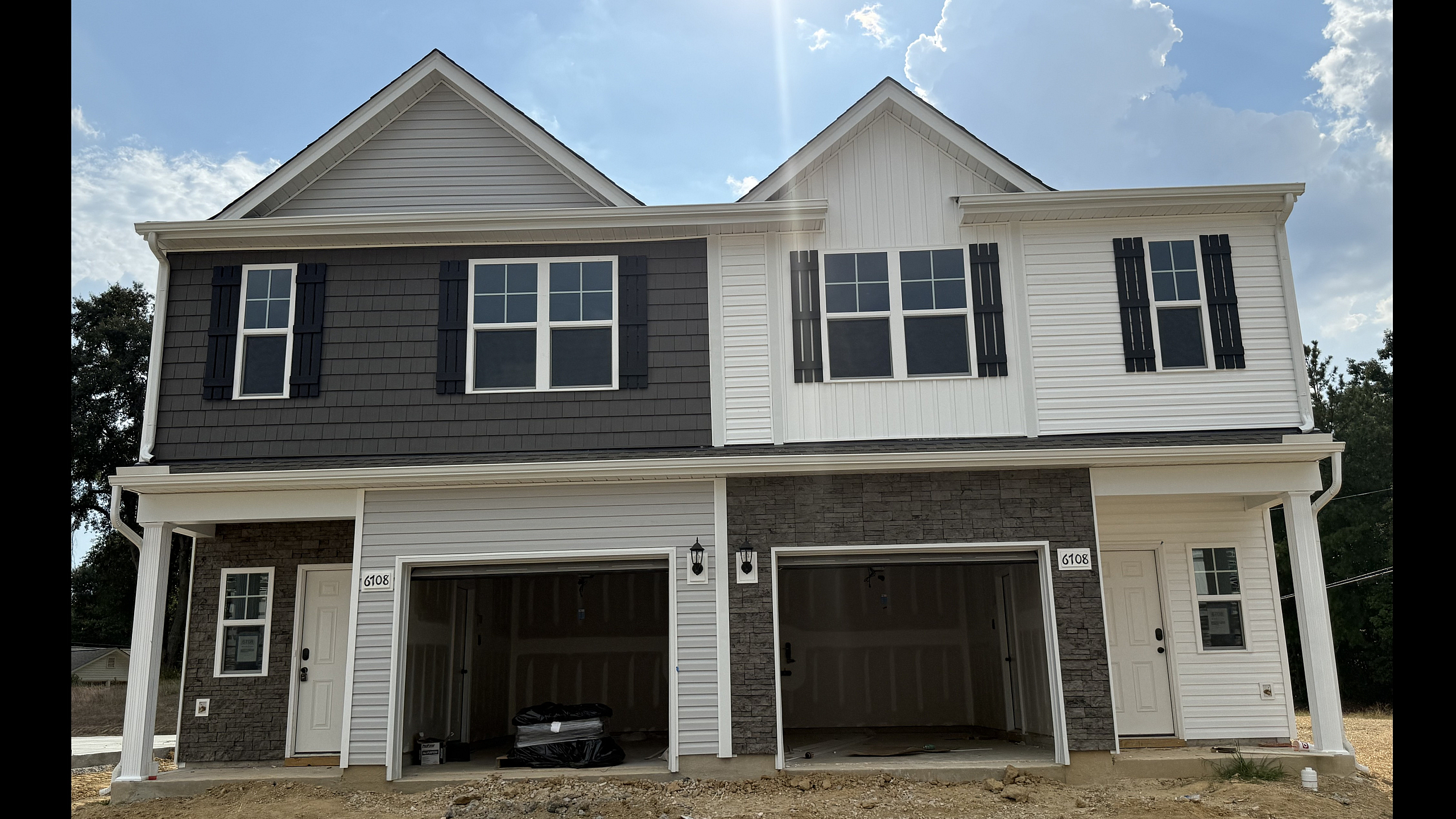 Elegant two-story duplex showcasing a modern exterior with contrasting siding, spacious dual garages, and inviting entryways under a bright blue sky.