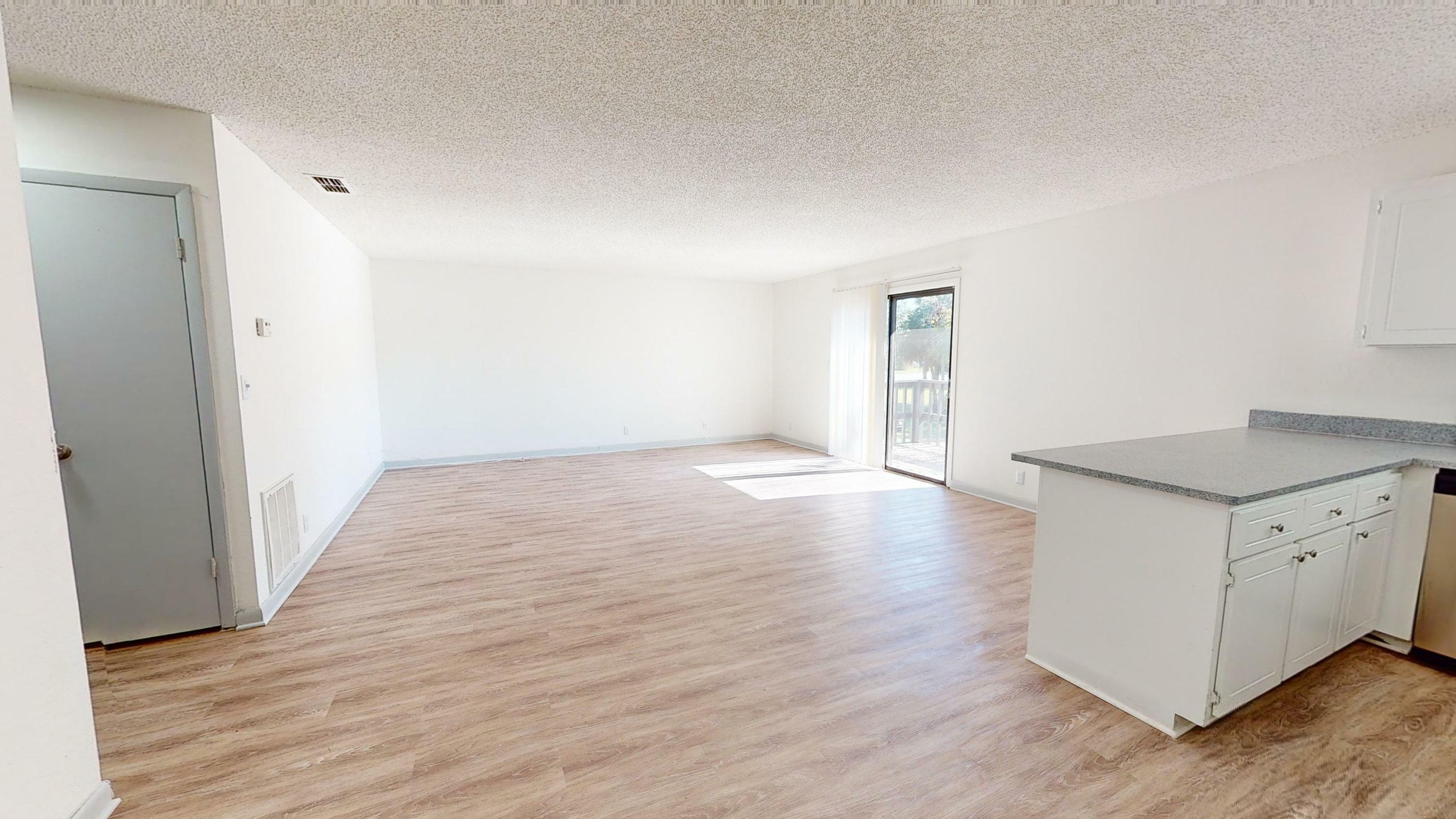 Inviting open-concept living room with wooden flooring, ample natural light, and a modern kitchen corner.