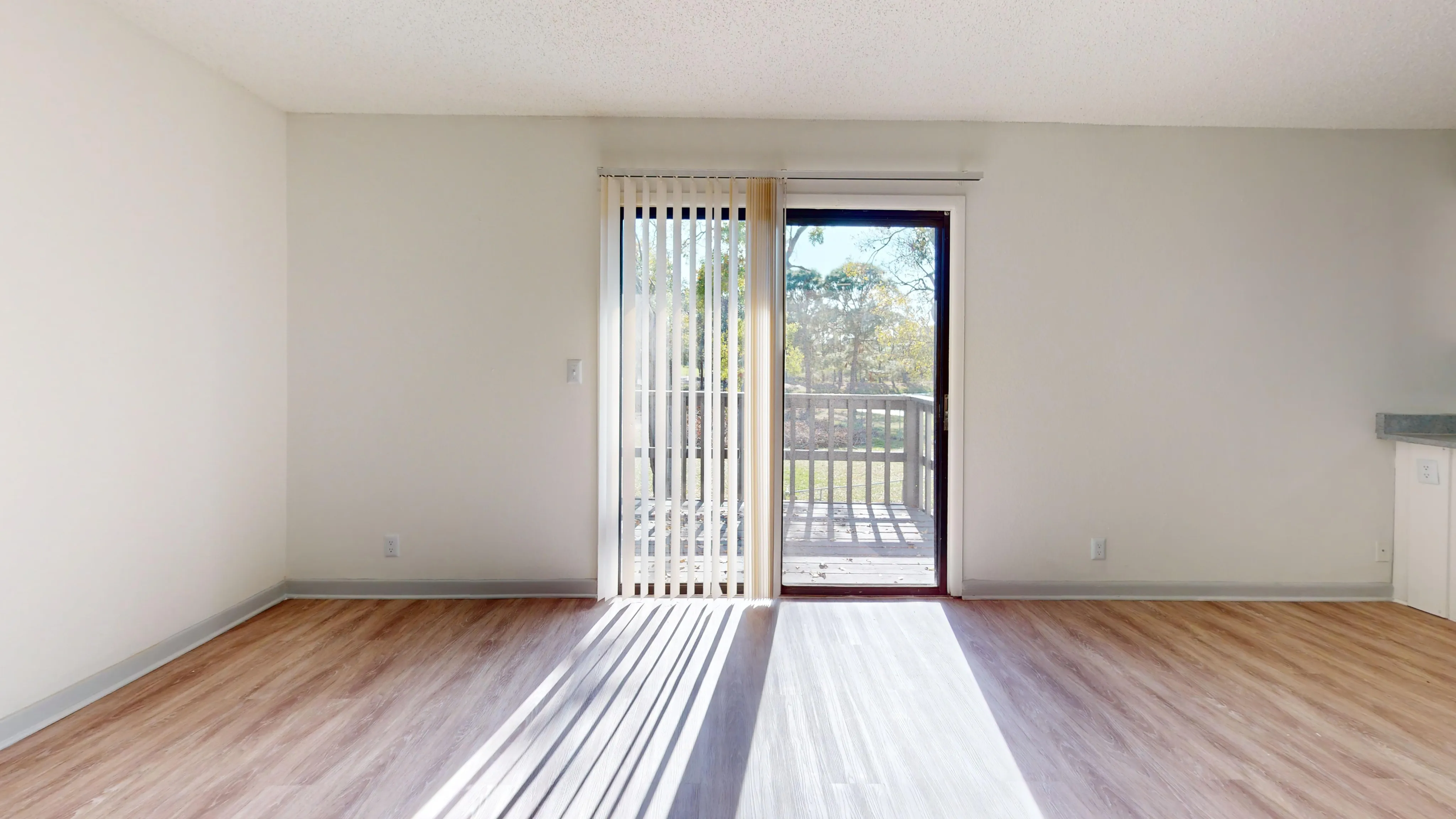 Spacious and bright living room with wooden flooring and sliding doors leading to a balcony.