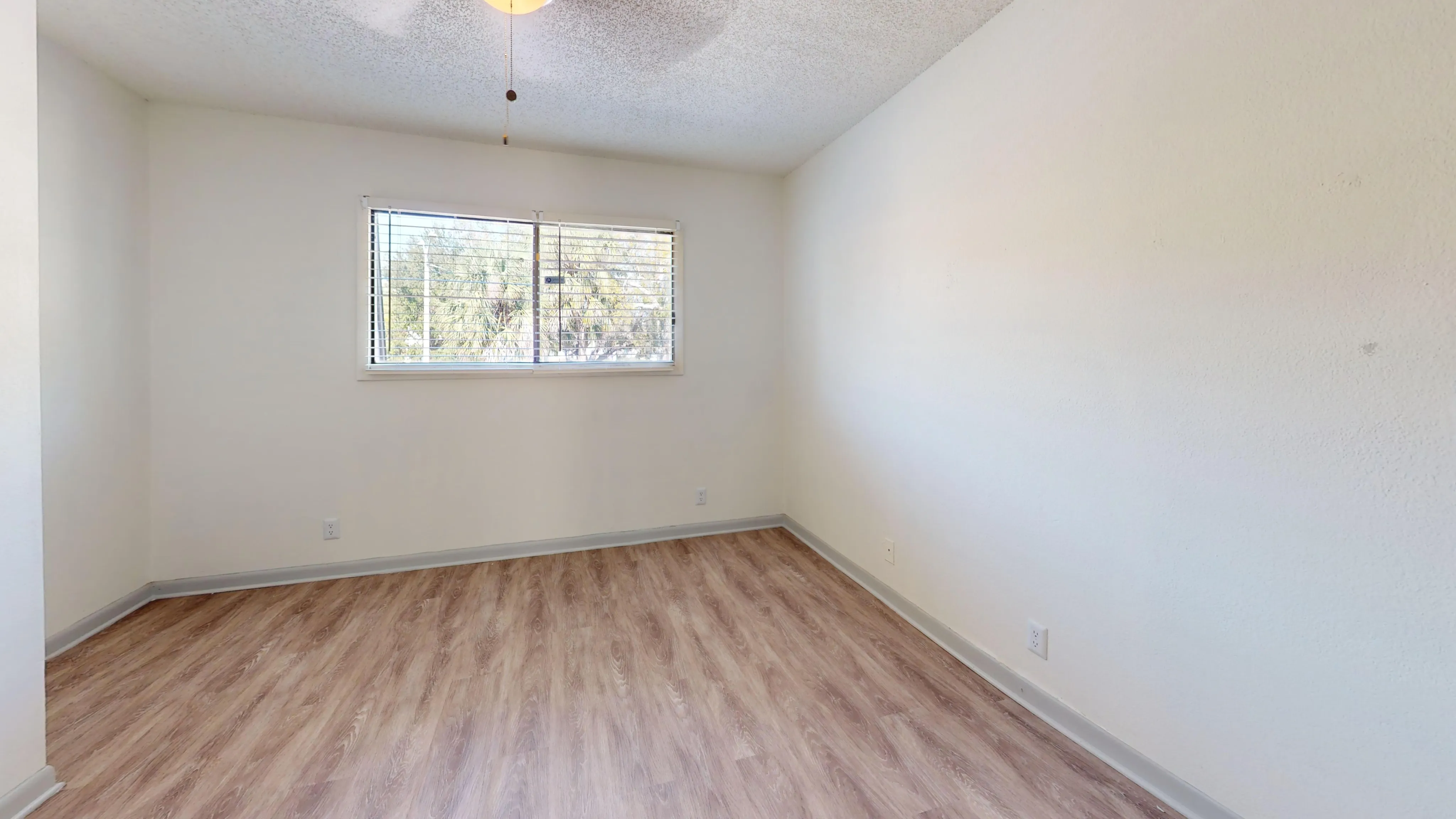 Sunny room with light wood flooring and a large window, ideal for a cozy bedroom setup.