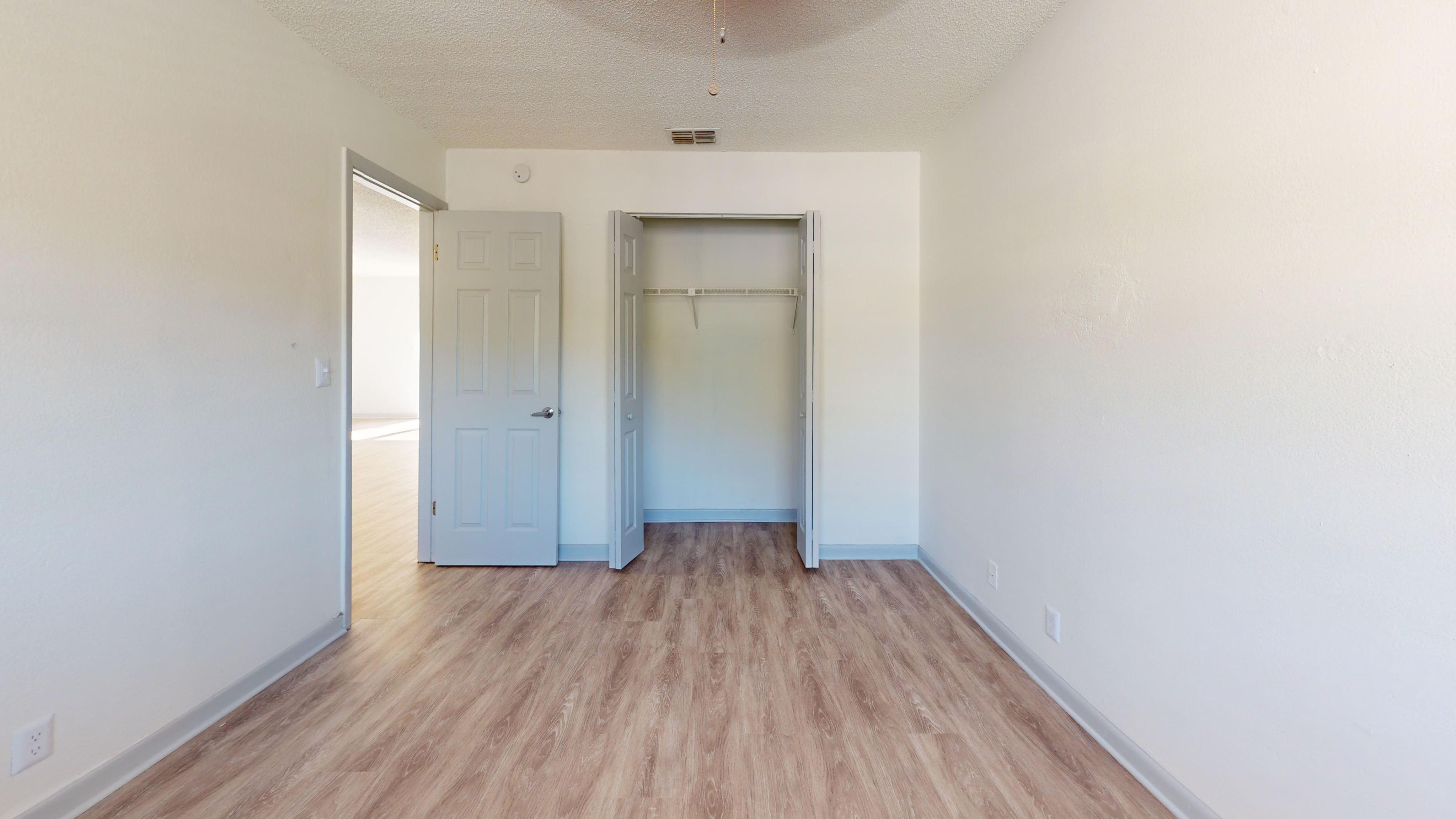 Spacious bedroom with wood flooring, open double door closet, and ample natural lighting.