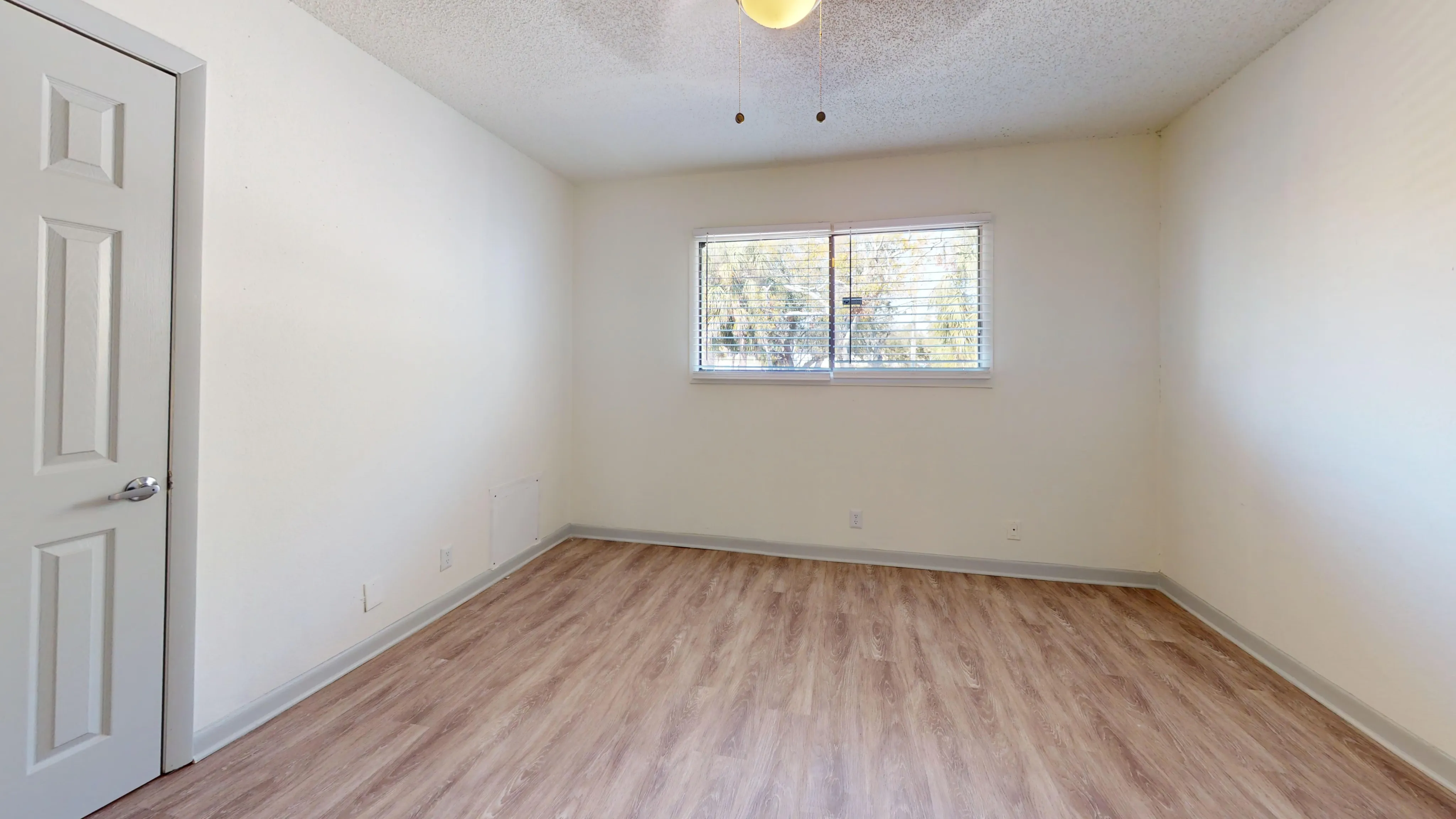 Spacious empty bedroom with wood flooring and large window providing natural light.