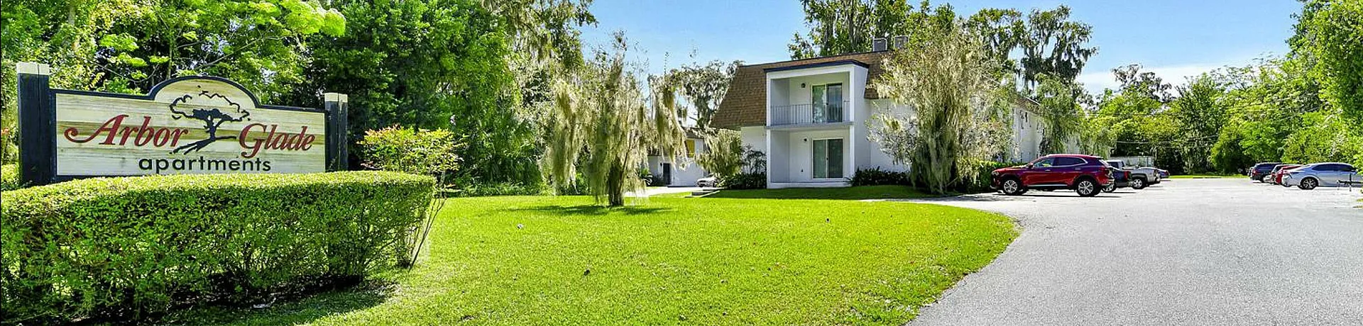 Charming exterior view of Arbor Glade Apartments surrounded by lush greenery and bright blue skies.
