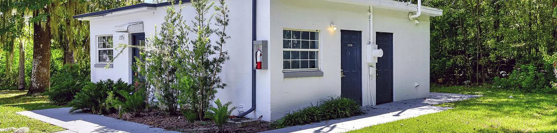 Charming single-story white cottage with lush greenery and spacious lawn.