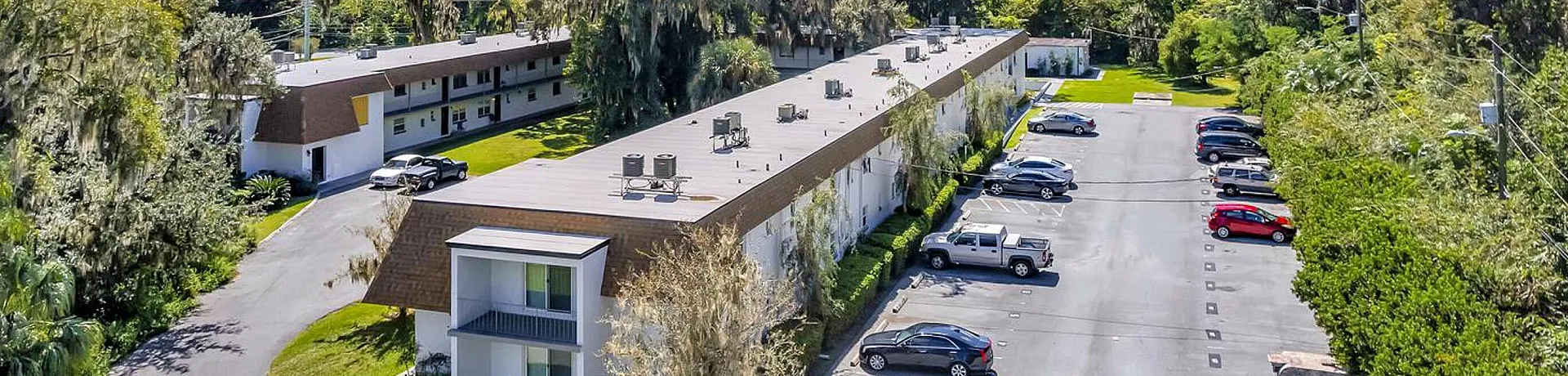 Aerial view of a spacious apartment complex surrounded by lush greenery and ample parking.