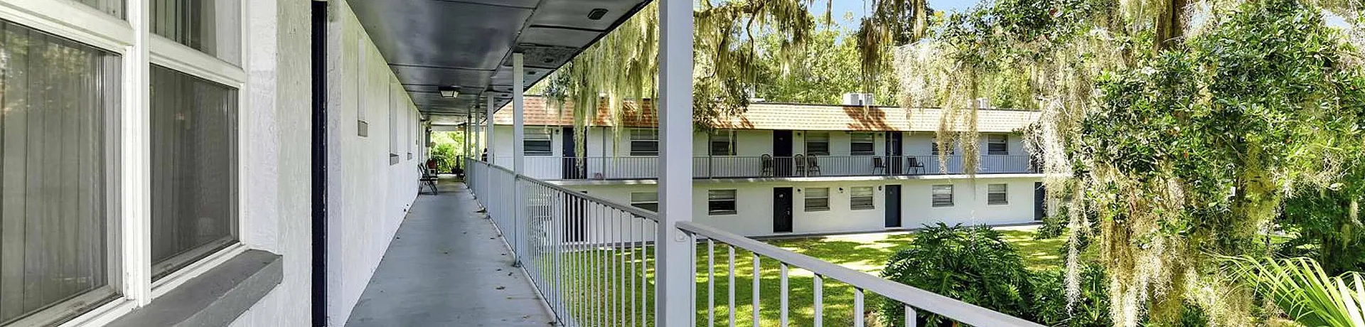Peaceful covered apartment walkway with a view of lush green courtyard.