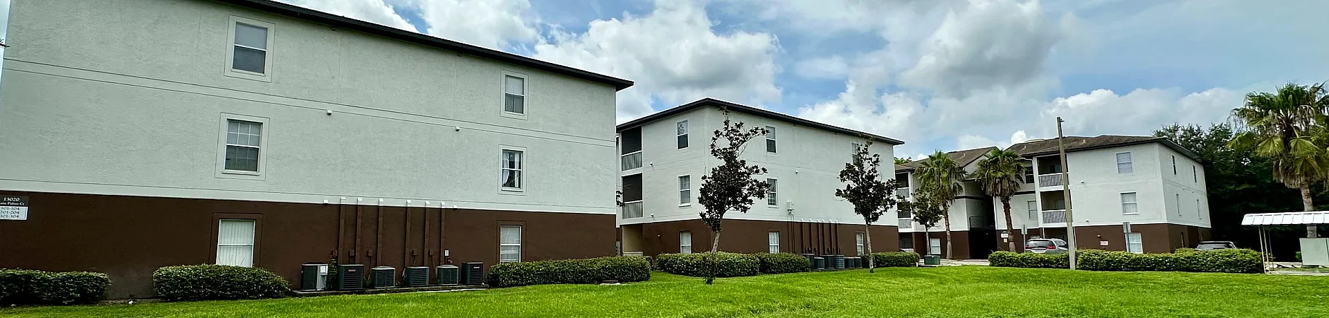 Charming apartment complex with lush green surroundings and spacious open areas under a picturesque sky.