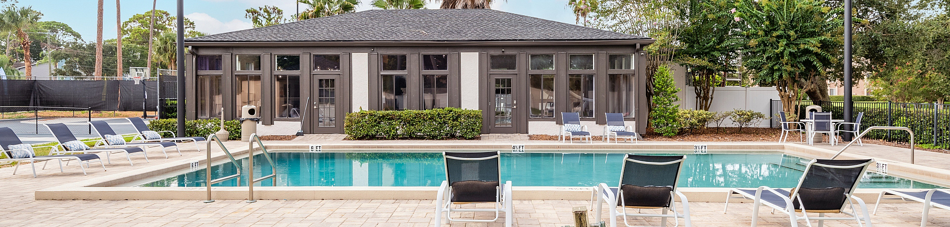 Luxurious apartment community showcasing a pristine swimming pool, elegant lounge chairs, and a stylish clubhouse surrounded by lush greenery.