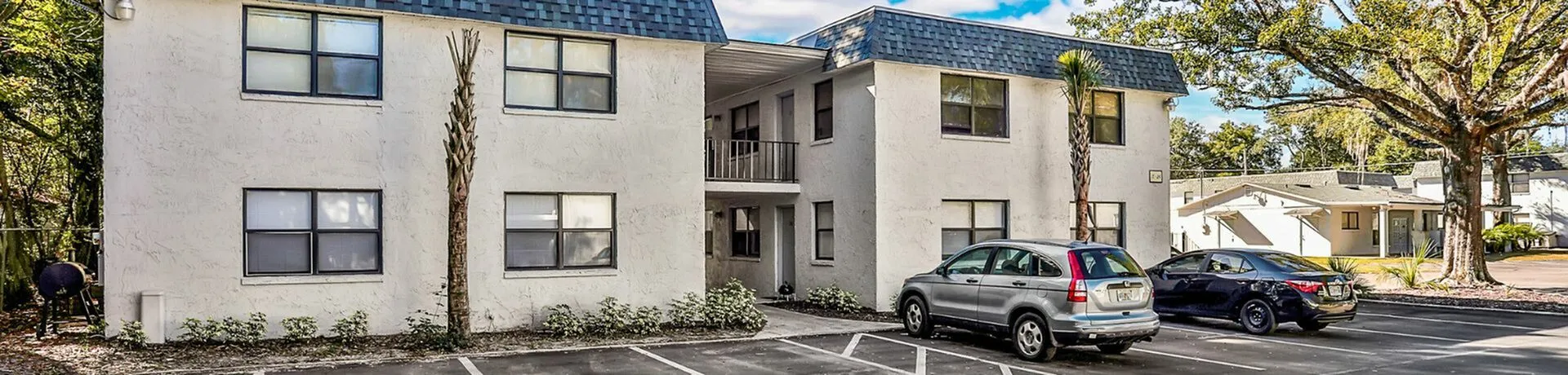 Charming two-story apartment building with lush greenery, ample parking, and a welcoming exterior.