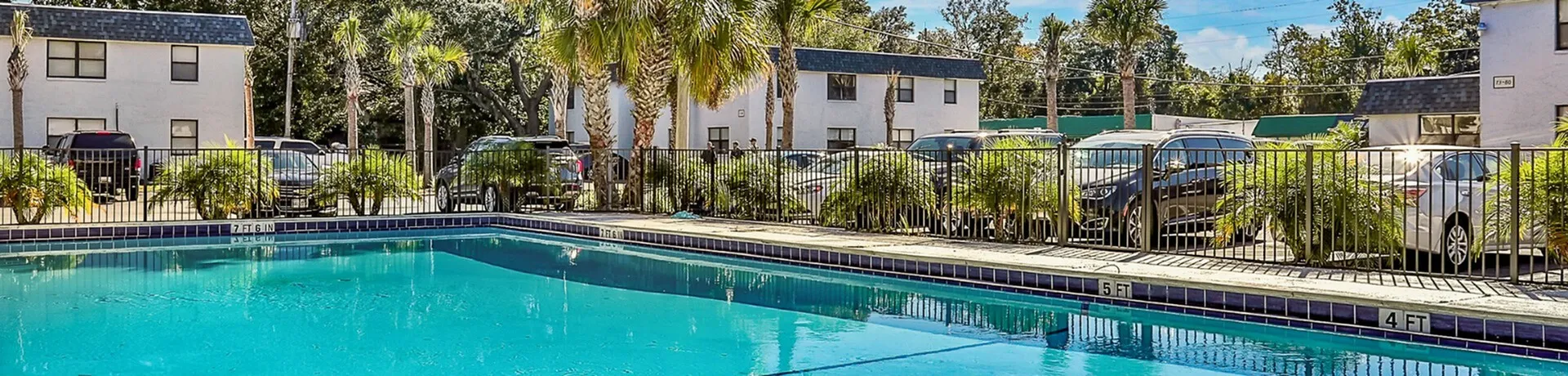 Inviting outdoor swimming pool with sunlit water, surrounded by lush palm trees in a vibrant apartment community.
