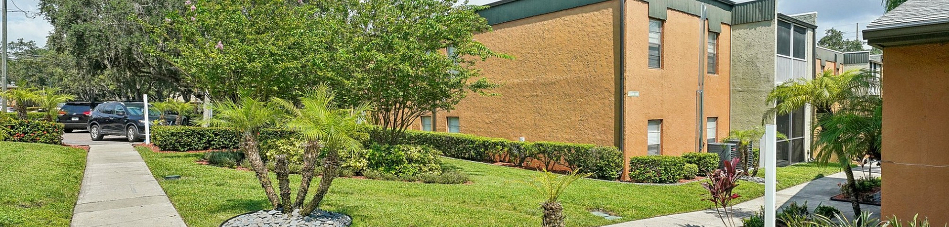 Charming apartment complex with well-maintained landscaping, featuring palm trees and lush greenery under a bright blue sky.