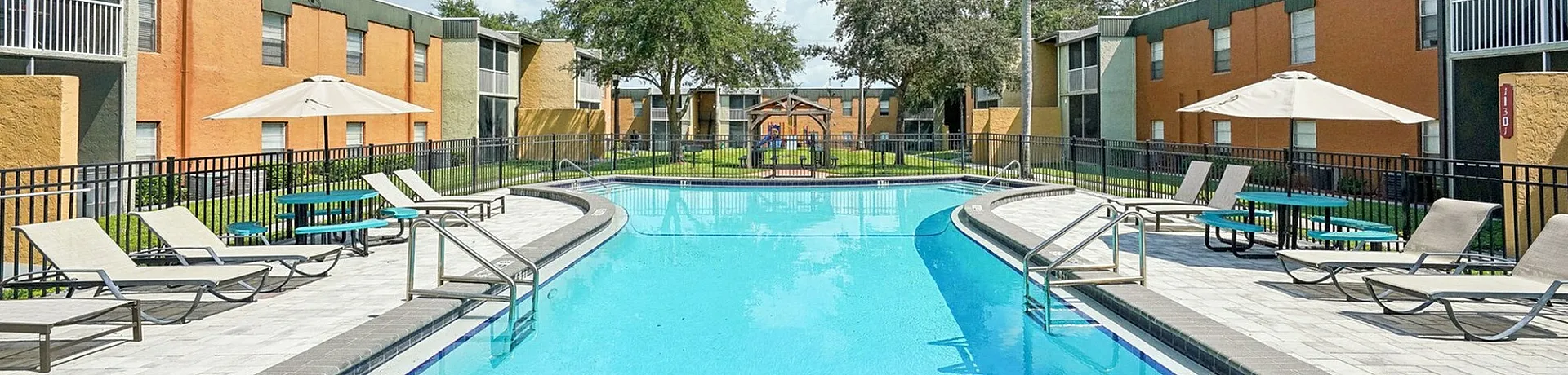 Vibrant apartment complex with a refreshing pool, sun loungers, and lush greenery offering a perfect relaxation spot.