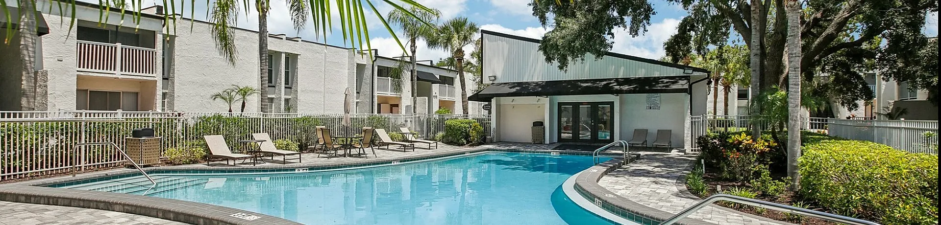 Luxurious apartment complex with a sparkling outdoor pool, surrounded by lush palm trees and inviting lounge chairs.