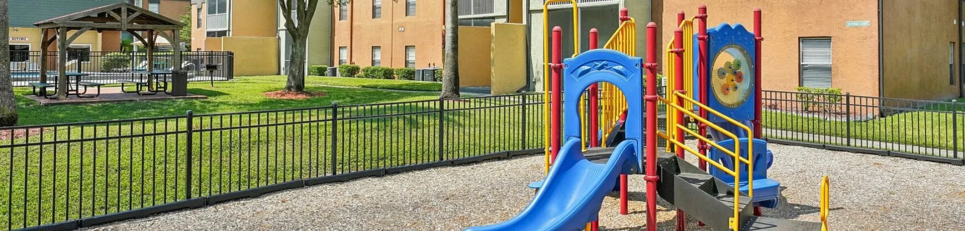 Charming apartment complex with a vibrant playground, lush trees, and a cozy gazebo area, perfect for families and outdoor enjoyment.