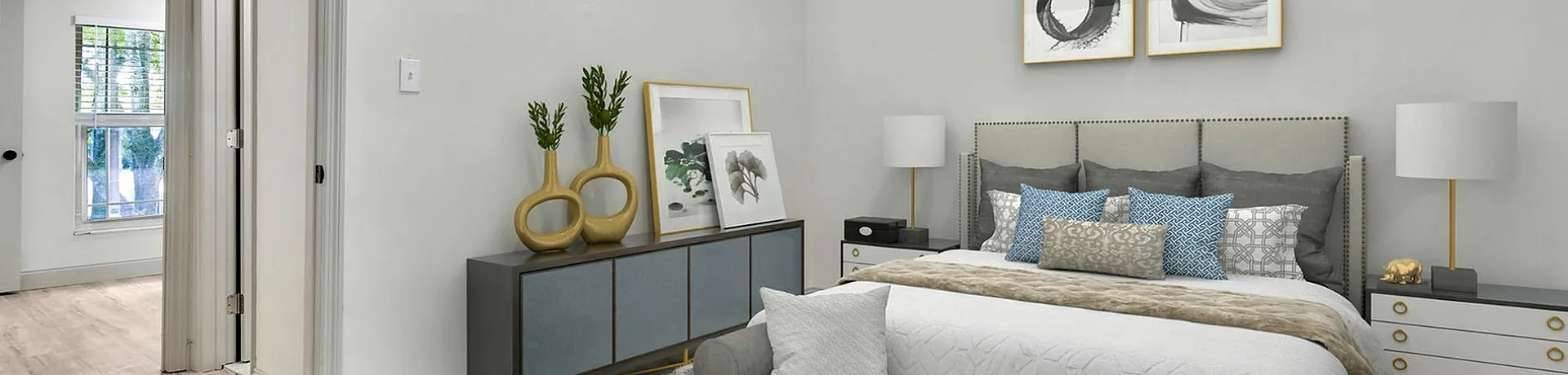 Elegant bedroom with cozy gray tones, plush bedding, stylish artwork, and natural light streaming through large windows.