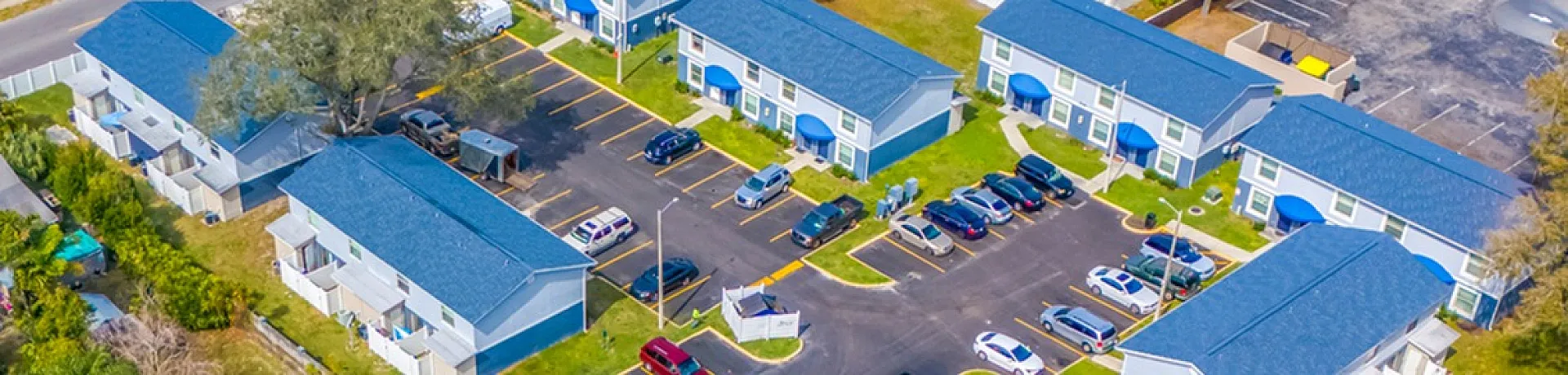 Charming aerial view of a vibrant apartment complex with blue-roofed buildings, lush greenery, and a sparkling pool, offering an attractive and serene living environment.