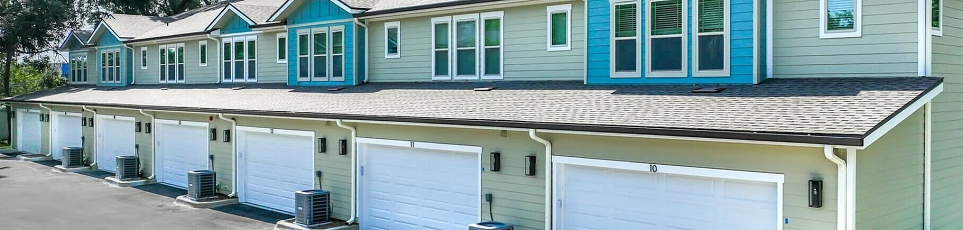 Charming townhouse complex with modern architecture, spacious driveways, and lush greenery on a sunny day.